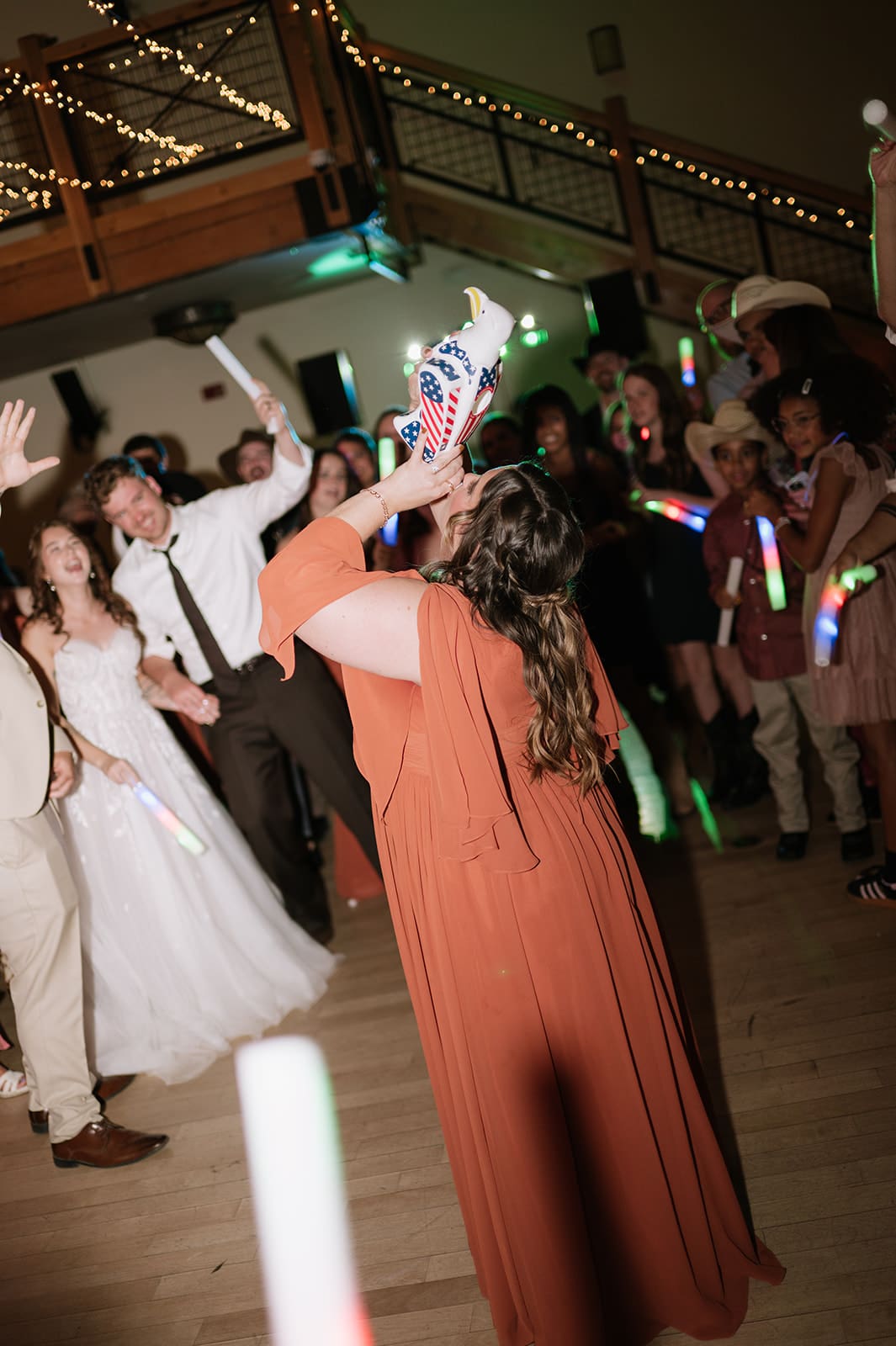 A group of people dance together on a crowded dance floor, surrounded by guests waving glow sticks.
