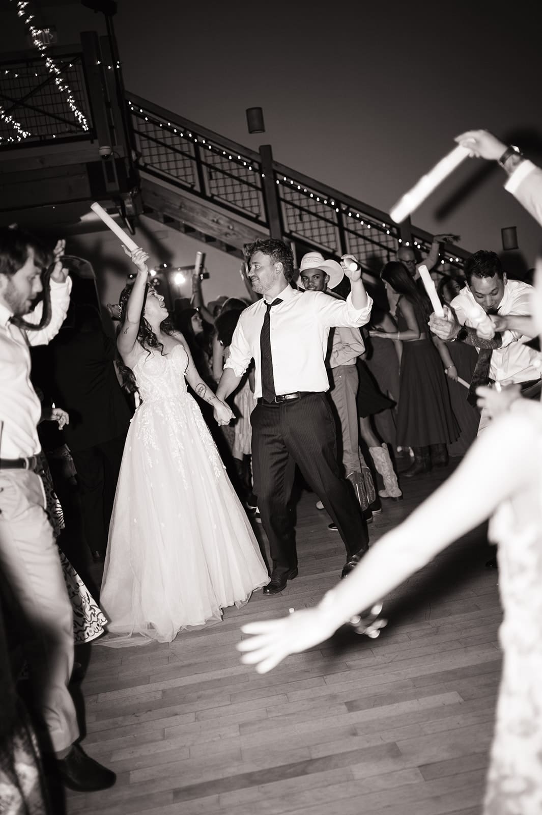 A bride and groom dance together on a crowded dance floor, surrounded by guests waving glow sticks.
