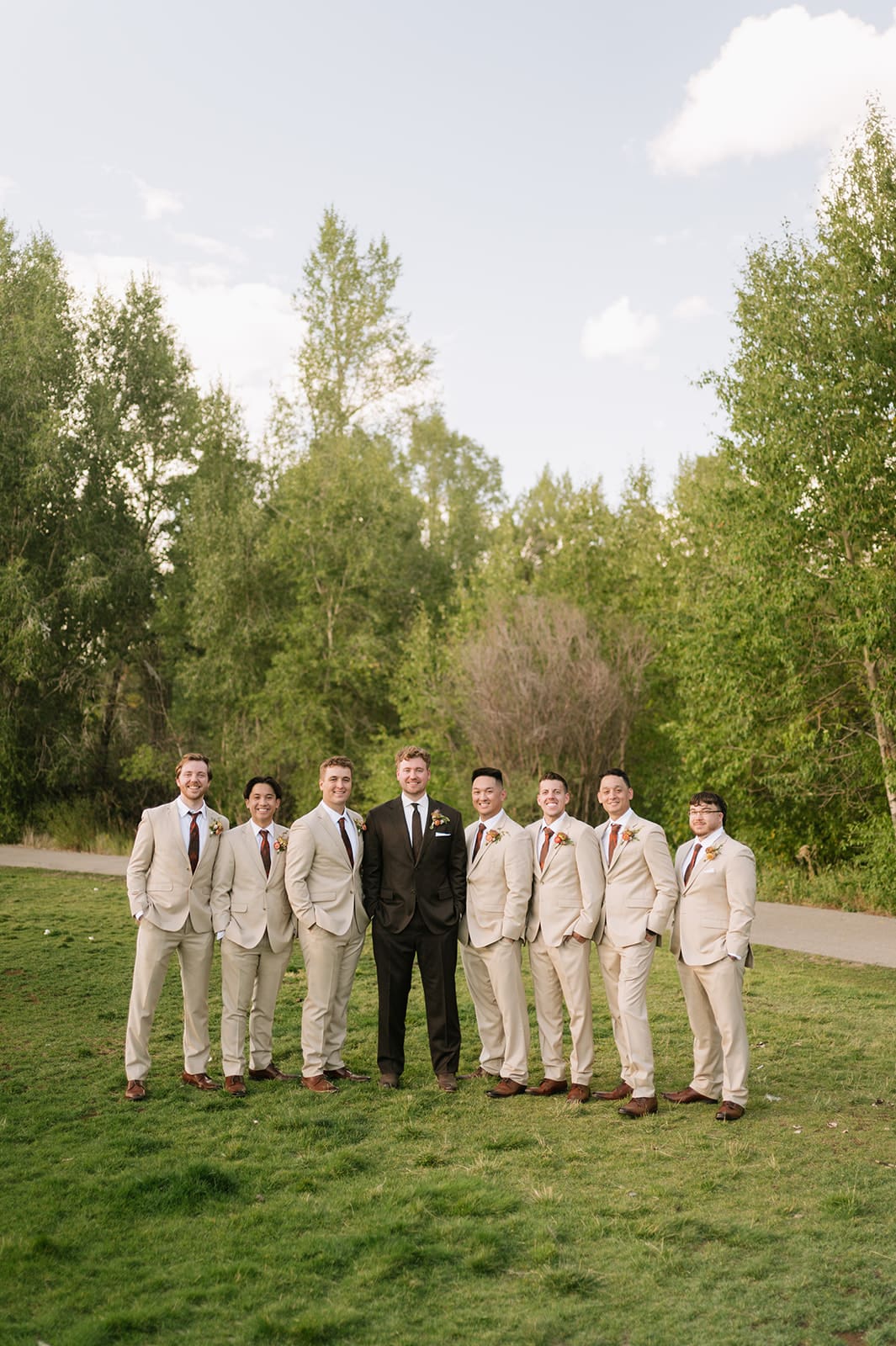 A group of seven men standing on grass, six in light-colored suits and one in a dark suit, talking and smiling outdoors.