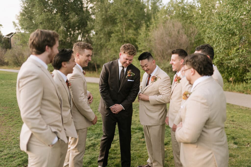 A group of seven men standing on grass, six in light-colored suits and one in a dark suit, talking and smiling outdoors.