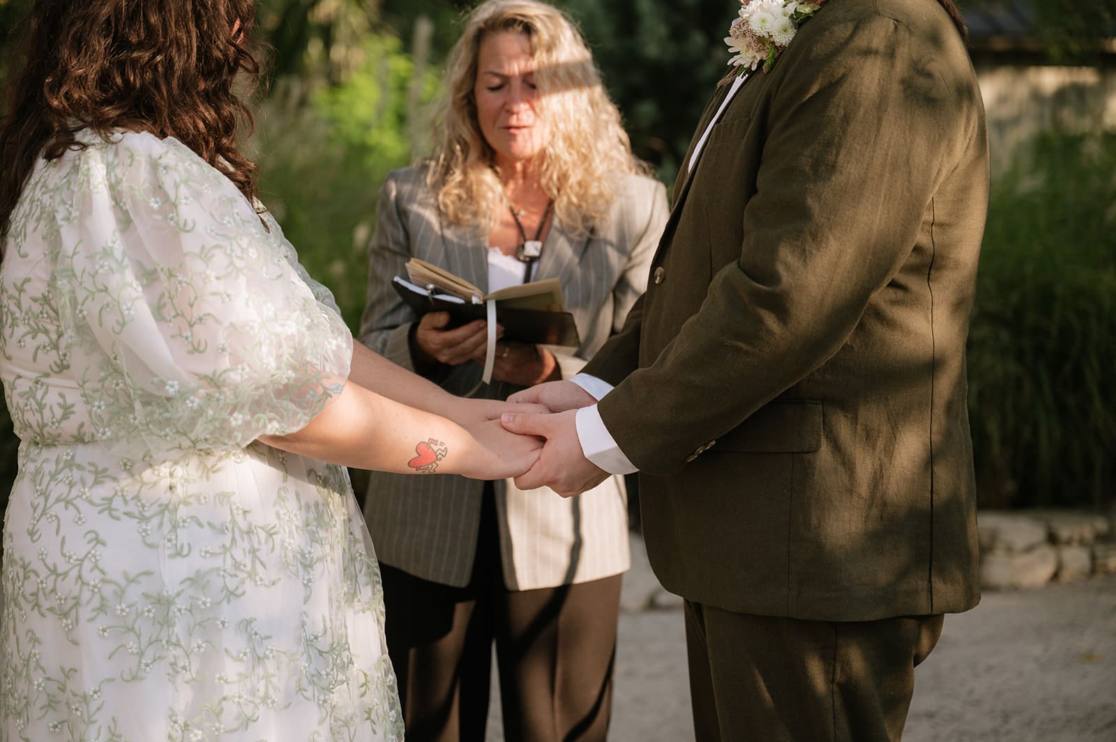 Two people stand facing each other outdoors under a leafy archway; one is holding a piece of paper and appears to be speaking for a texas hill country elopement
