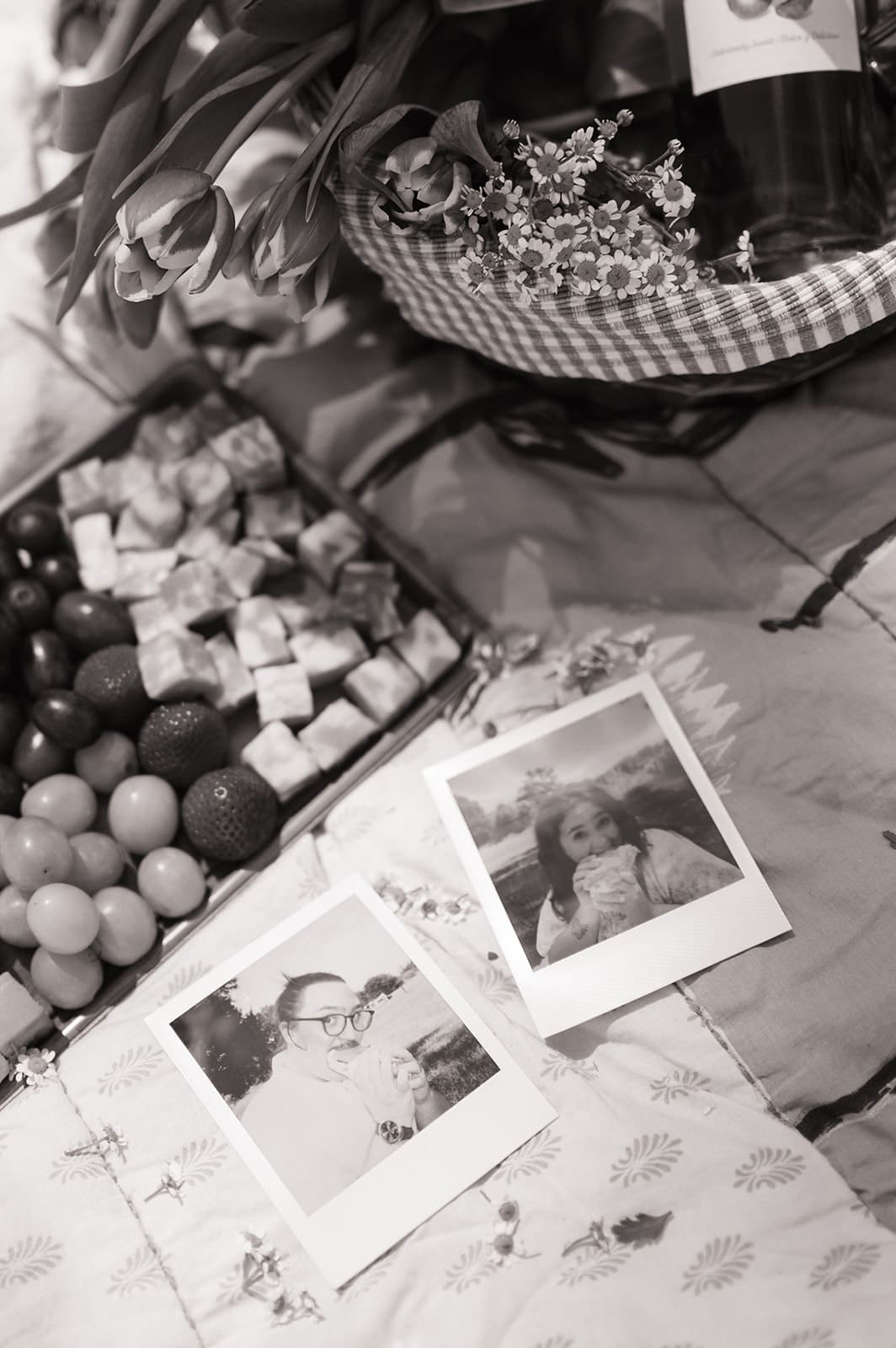 Two people sit on a blanket having a picnic outdoors, surrounded by greenery, with food and flowers arranged between them for a Texas Hill Country Elopement