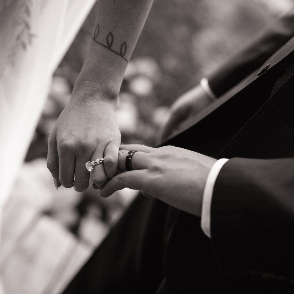 Two people exchange rings during a wedding ceremony, one wearing a suit and the other wearing a dress, shown in black and white.