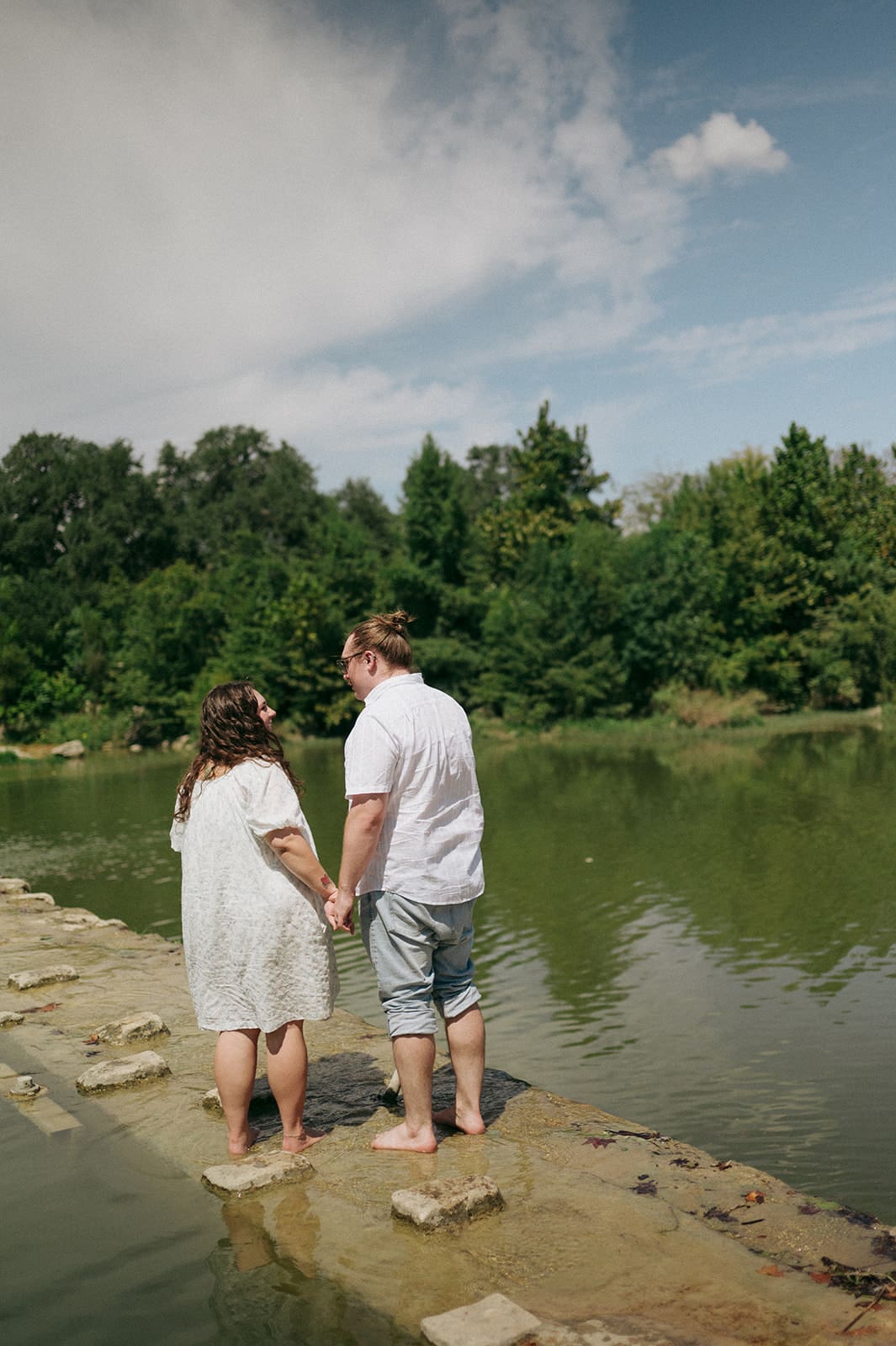Two people sit on a blanket having a picnic outdoors, surrounded by greenery, with food and flowers arranged between them for a Texas Hill Country Elopement