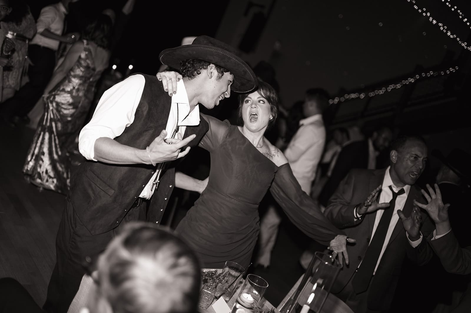 A group of people dance together on a crowded dance floor, surrounded by guests waving glow sticks.