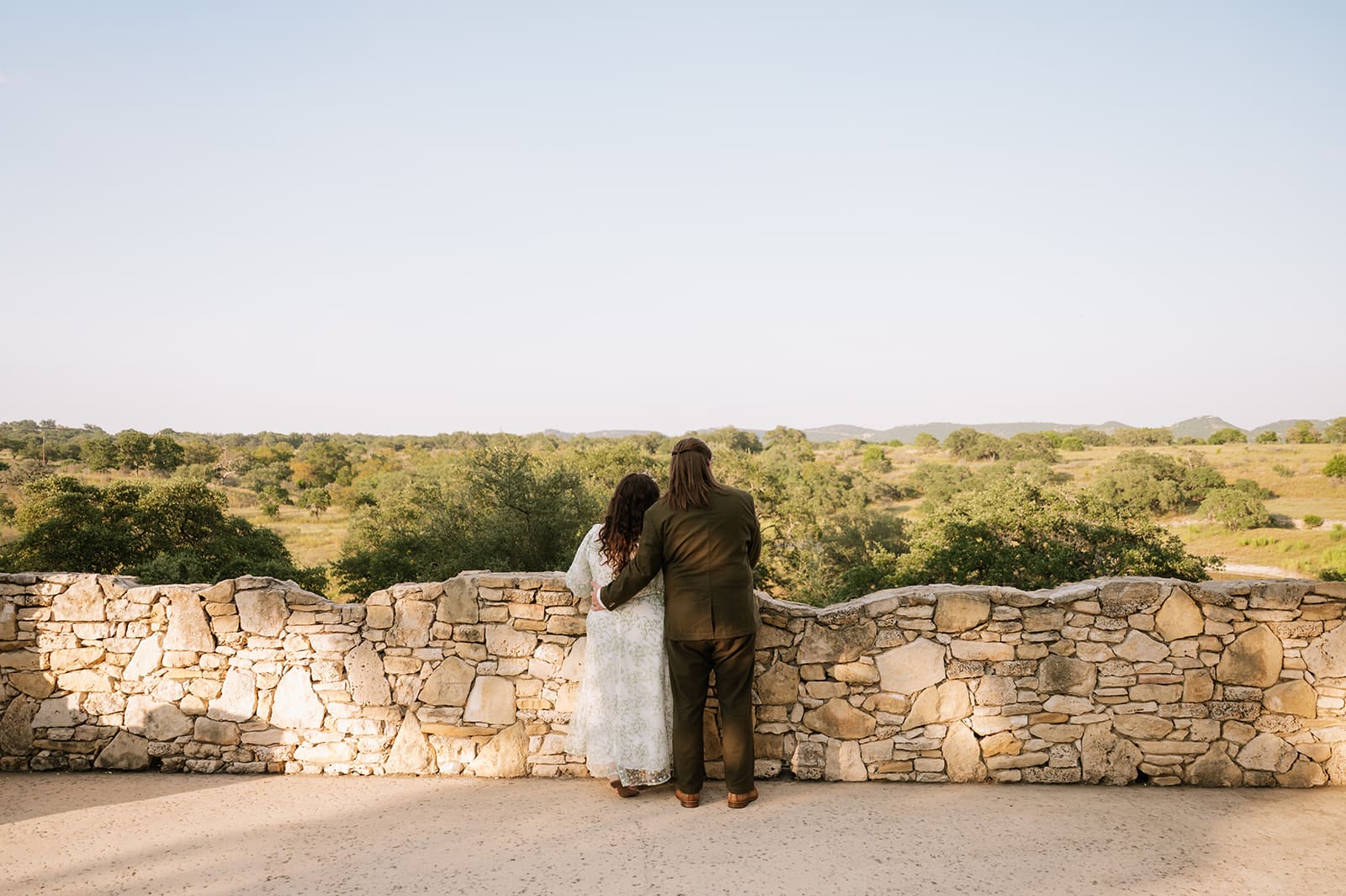 A couple dressed in formal attire takes elopement photos while standing outdoors on a sunny day for a texas hill country elopement