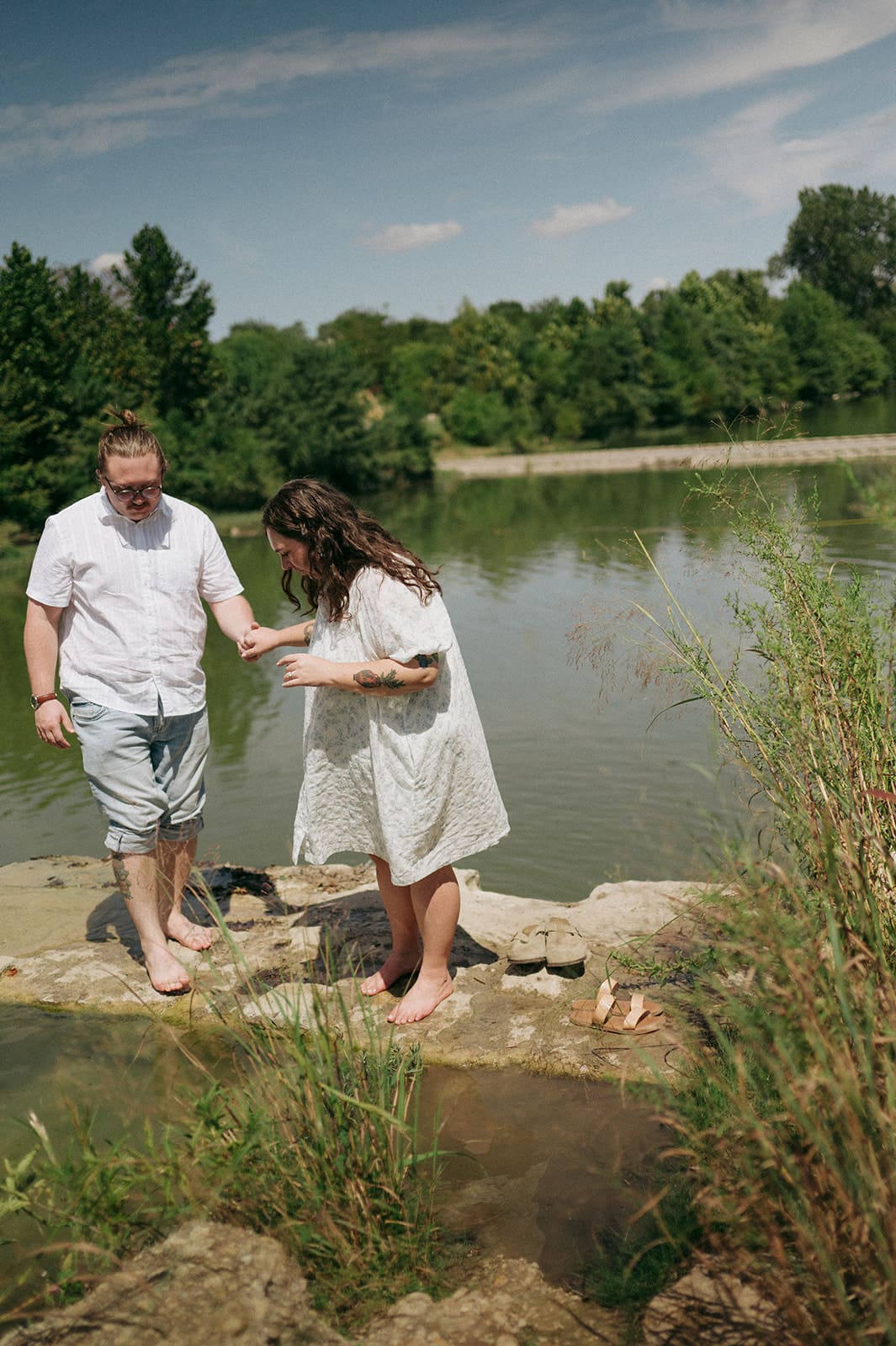 Two people sit on a blanket having a picnic outdoors, surrounded by greenery, with food and flowers arranged between them for a Texas Hill Country Elopement