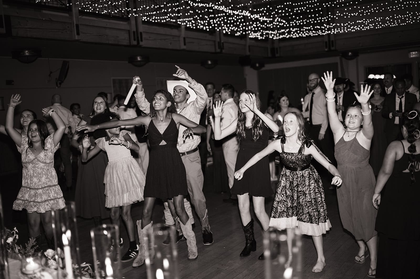 A group of people dance together on a crowded dance floor, surrounded by guests waving glow sticks.