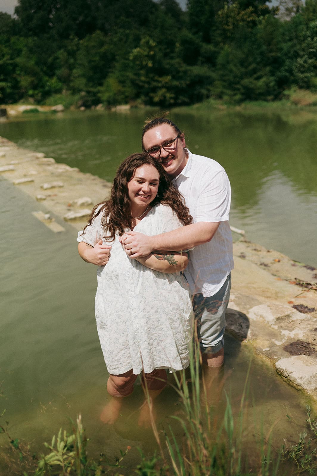Two people sit on a blanket having a picnic outdoors, surrounded by greenery, with food and flowers arranged between them for a Texas Hill Country Elopement