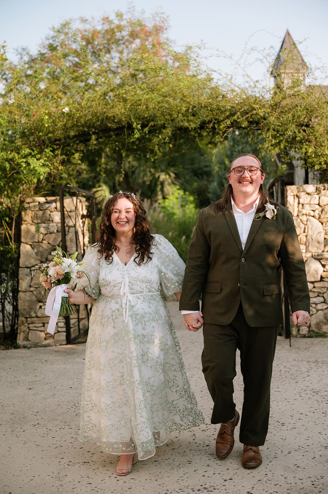 Two people stand facing each other outdoors under a leafy archway; one is holding a piece of paper and appears to be speaking for a texas hill country elopement