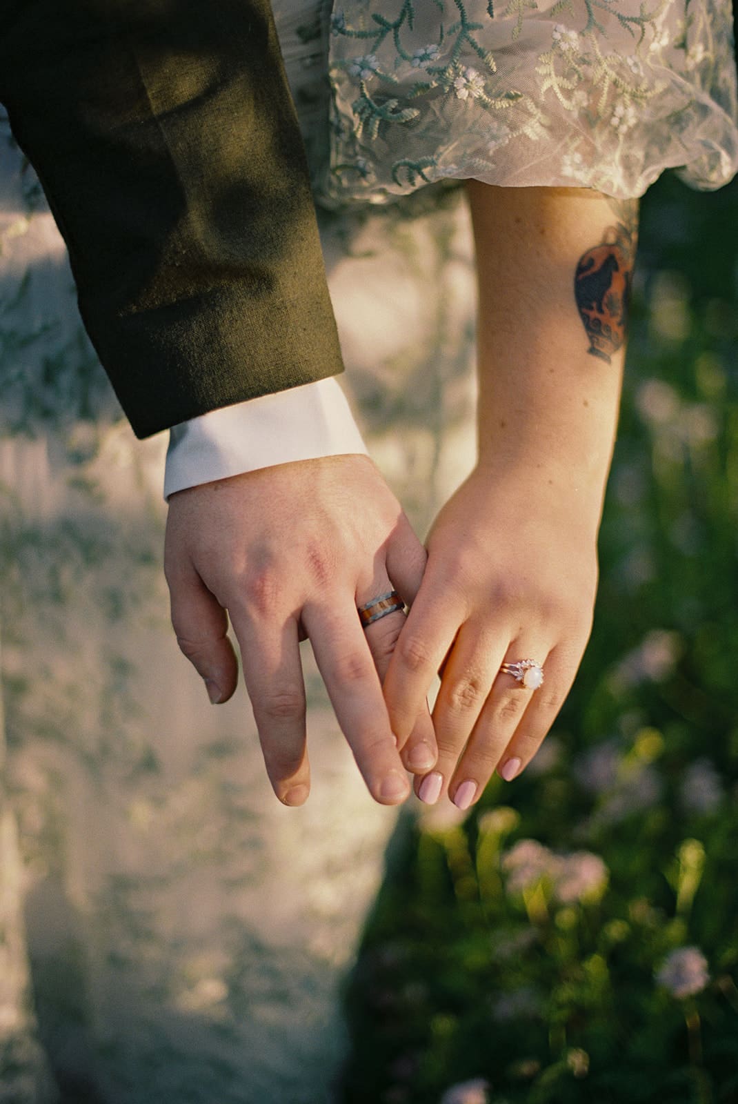 Two people in formal attire hold hands outdoors, both wearing rings. One person has a visible tattoo on their forearm for a texas hill country elopement 