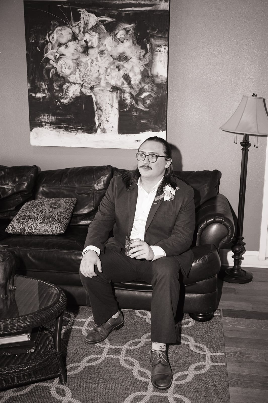 A woman sits on the floor in front of a mirror, styling her hair with both hands in a softly lit room.