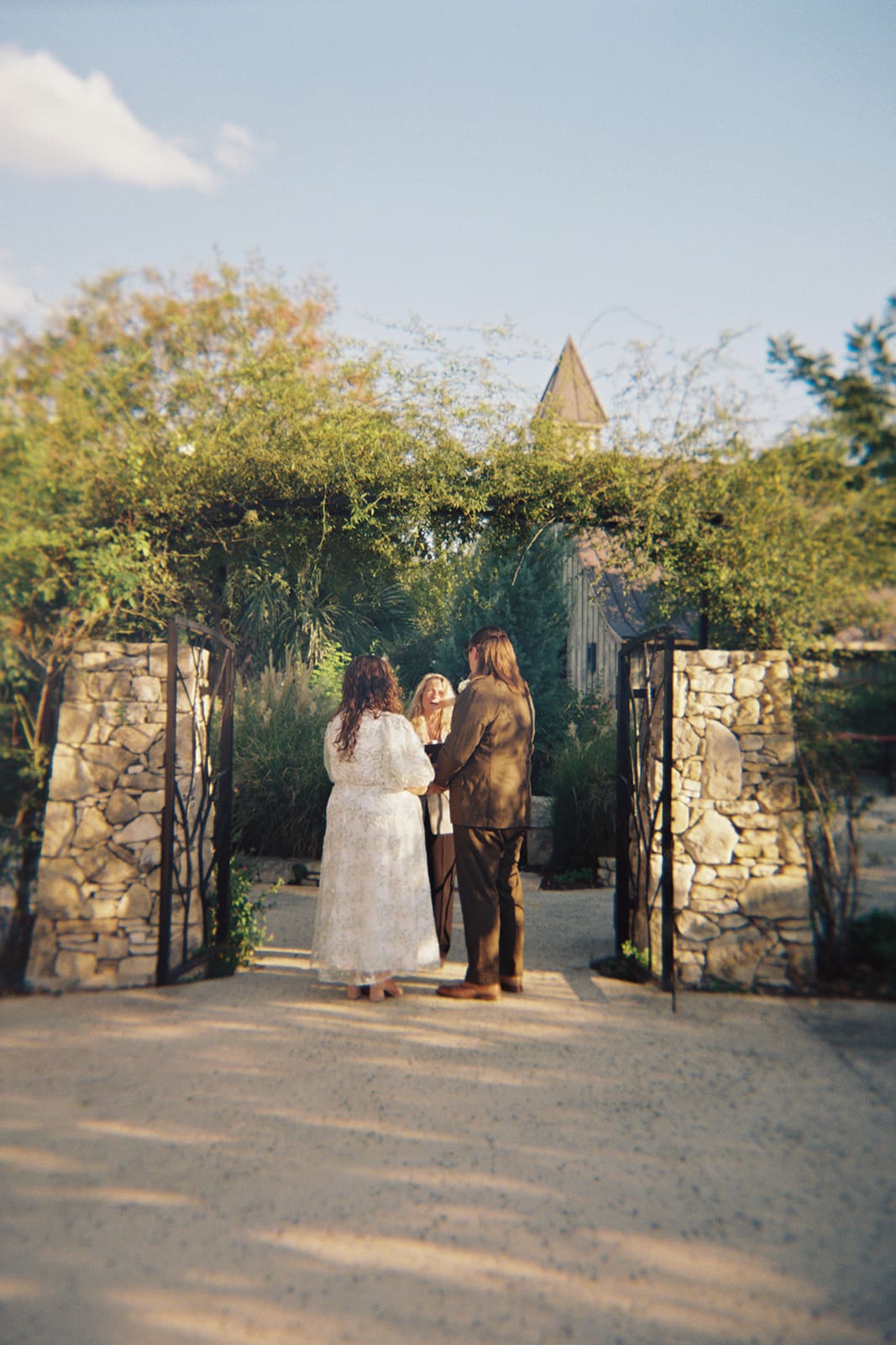 Two people stand facing each other outdoors under a leafy archway; one is holding a piece of paper and appears to be speaking for a texas hill country elopement