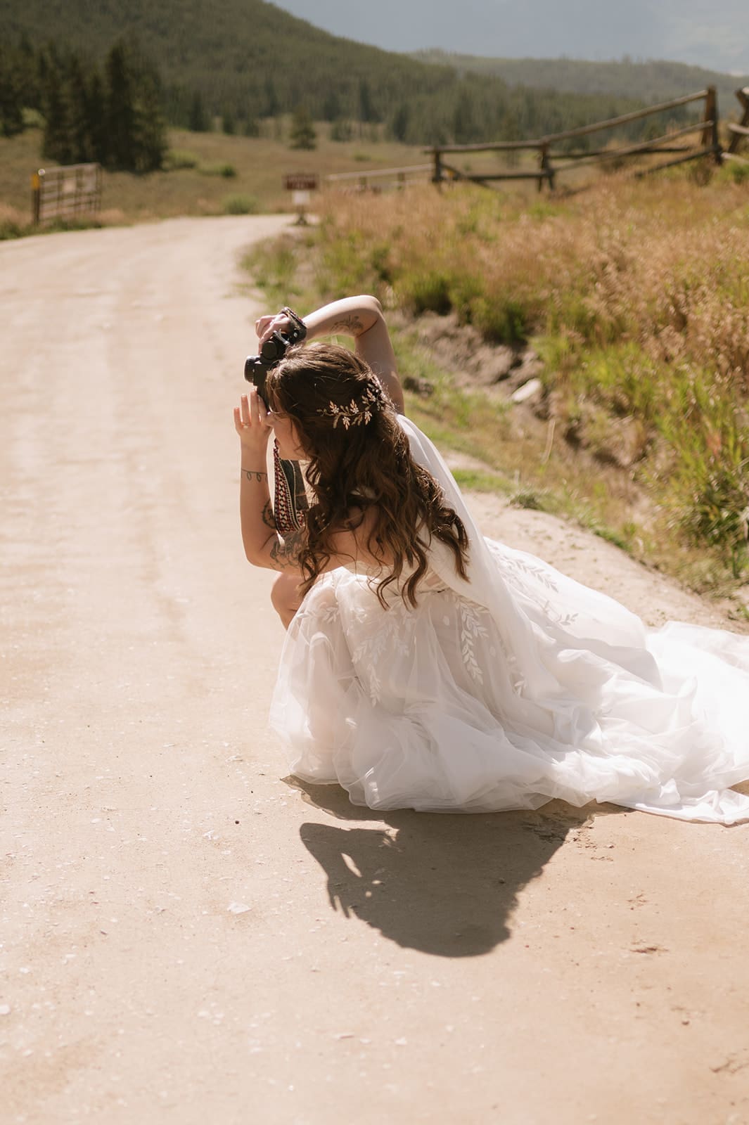 A bride and groom in wedding attire stand embracing on a rocky landscape with mountains and trees in the background under a partly cloudy sky for a Colorado wedding