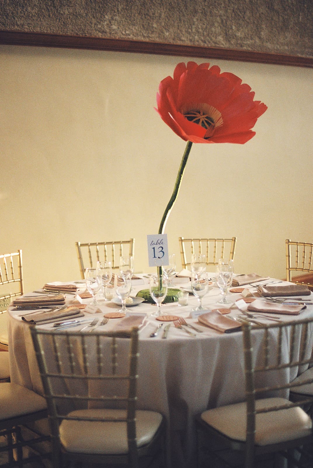 Elegant banquet hall with round tables, white chairs, oversized pink flower centerpieces, ornate stained-glass windows, and large circular chandeliers for a wedding at at The Ashton Depot in Fort Worth
