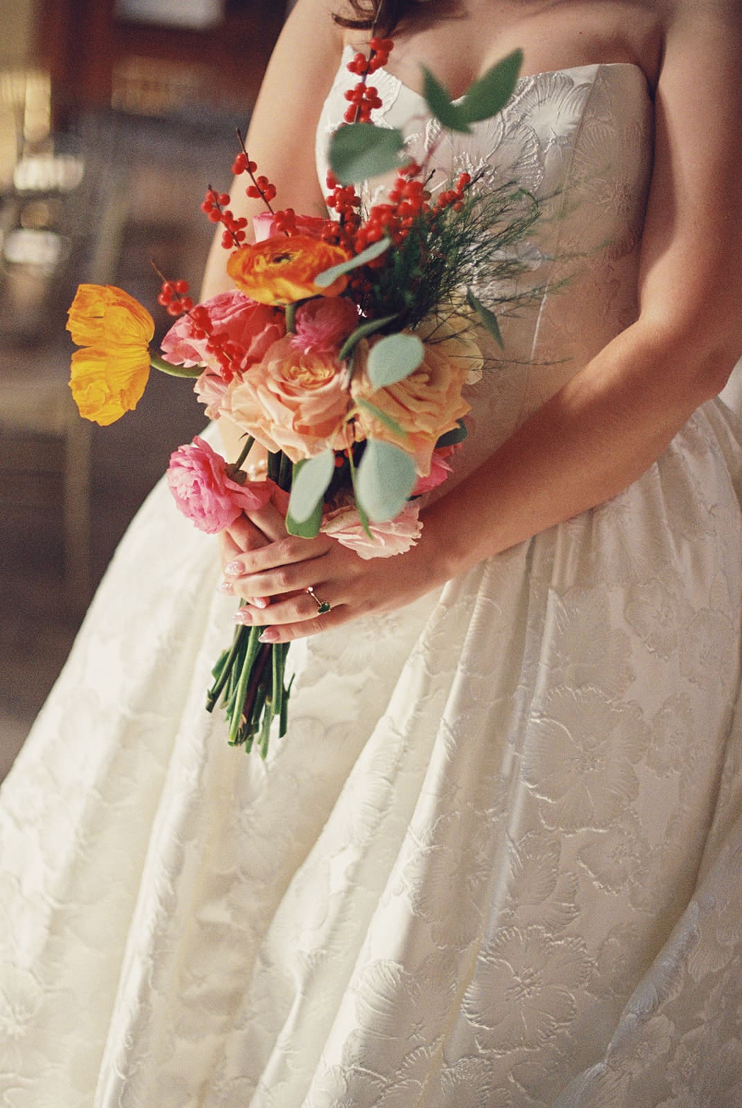 A bride in a white strapless wedding dress holds a colorful bouquet of flowers with red, orange, pink, and green foliage for a wedding at The Ashton Depot in Fort Worth