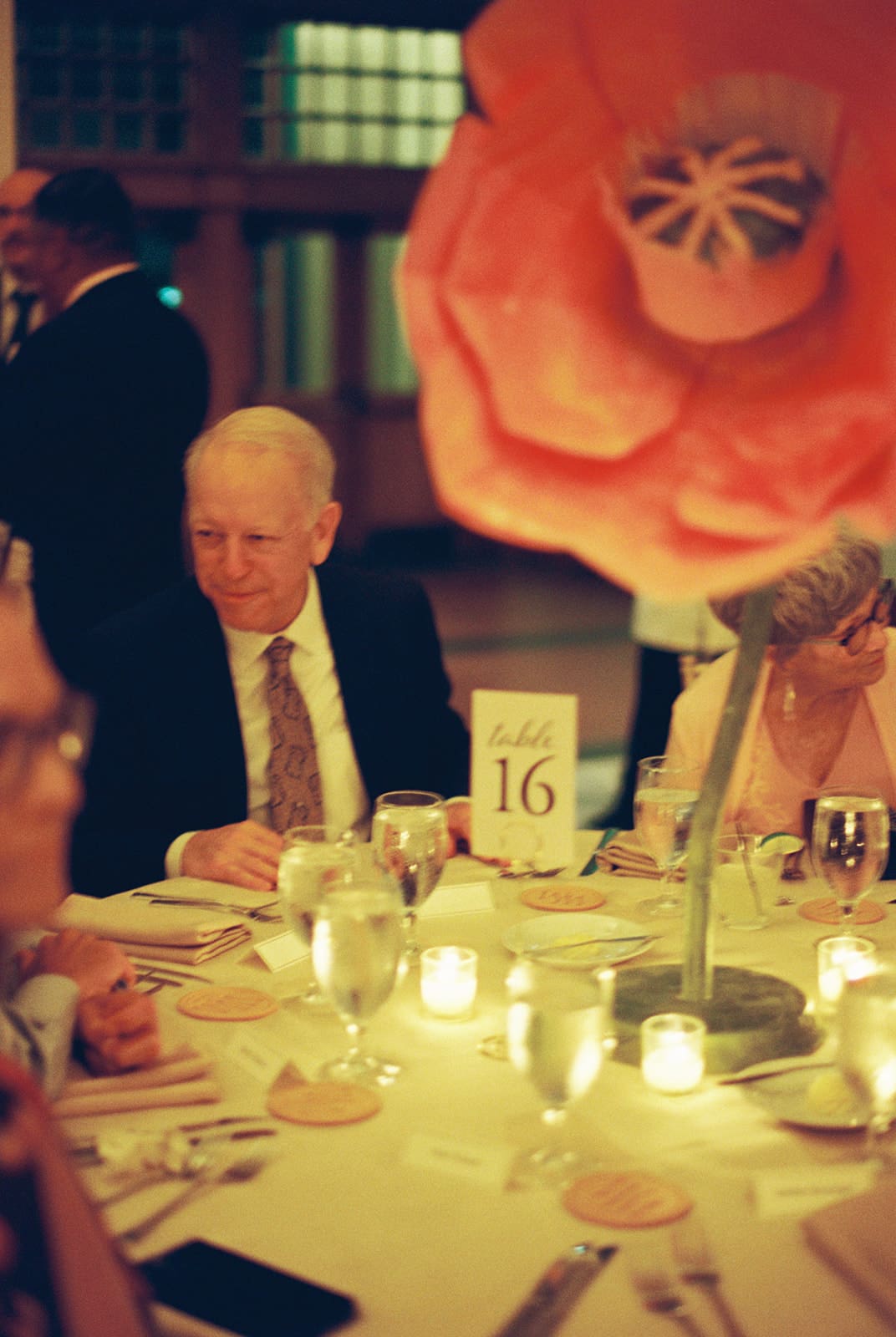 A banquet table set with glassware, plates, flower arrangements, and lit candles creating a warm, ambient glow.
