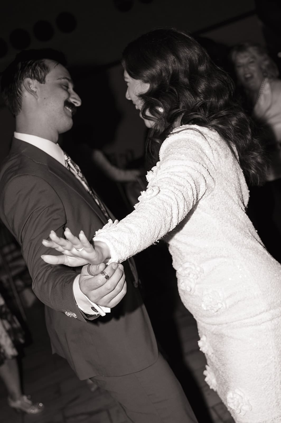 A man in a suit and a woman in a white dress are dancing together at an indoor event, smiling and holding hands for a Wedding at The Ashton Depot in Fort Worth, Texas