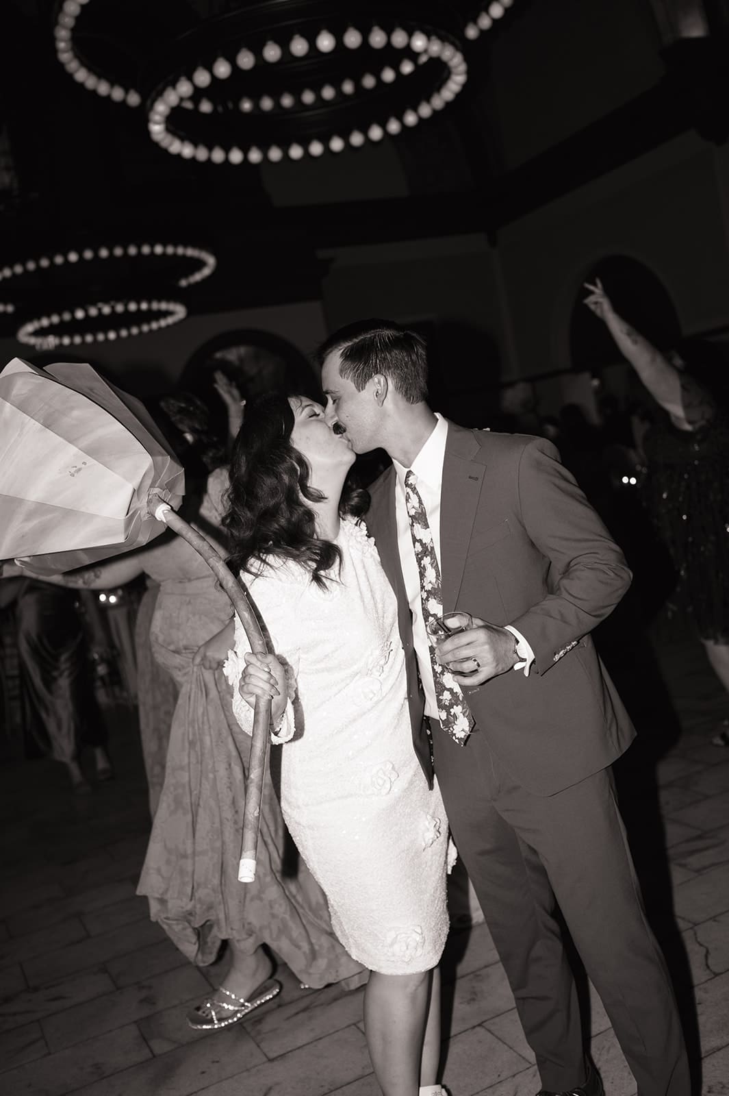 A man in a suit and a woman in a white dress are dancing together at an indoor event, smiling and holding hands for a Wedding at The Ashton Depot in Fort Worth, Texas