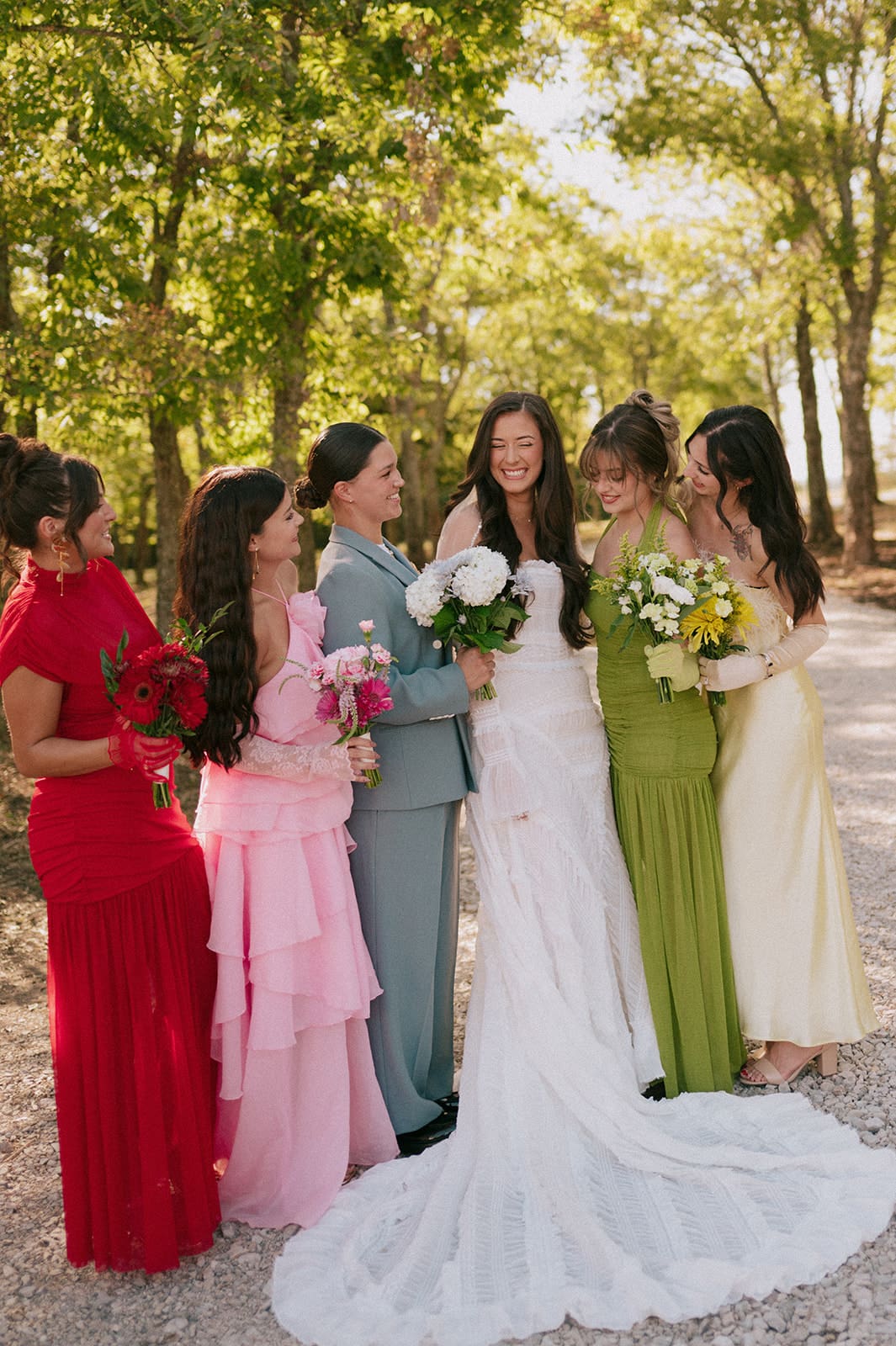 A group of six people, dressed in formal attire, stand together outdoors on a sunlit tree-lined path, smiling at the camera for a backyard wedding in Texas