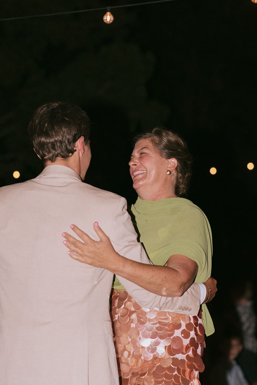 two people dance together outdoors at night under string lights for a backyard wedding in Texas