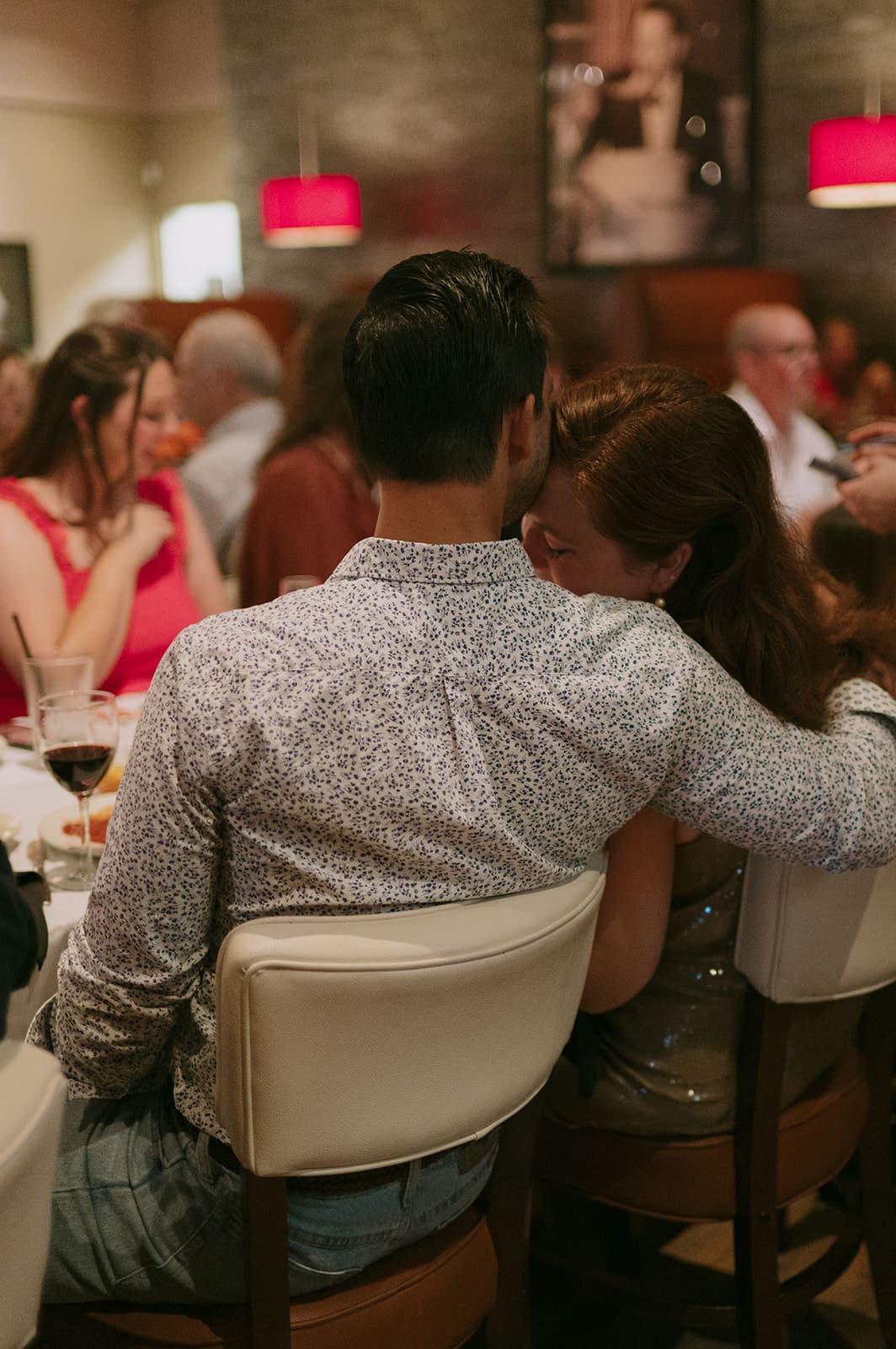 A group of four adults, dressed in semi-formal attire, stand together indoors and interact, smiling in a dimly lit room.