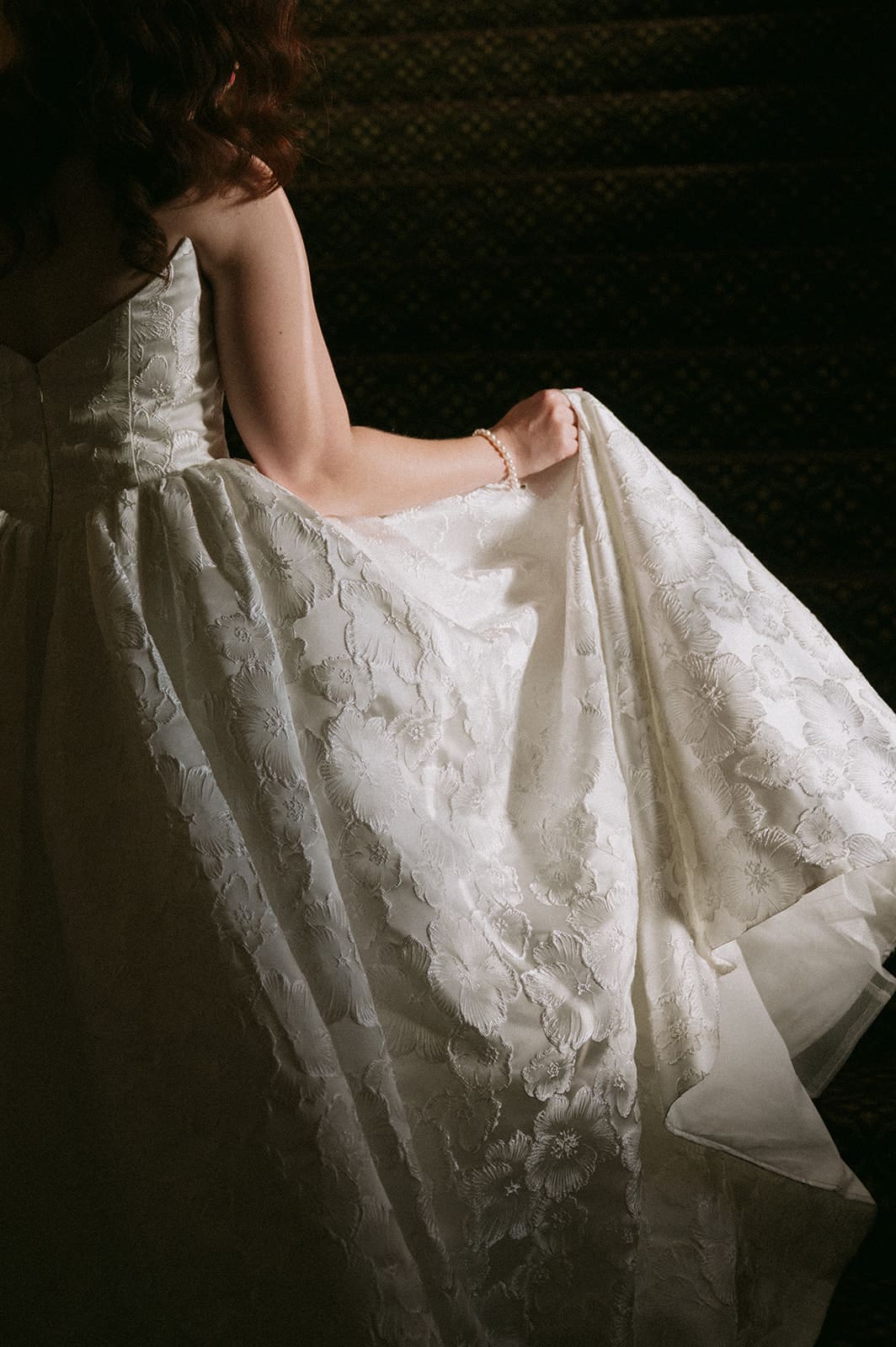 A person in a sleeveless, textured dress stands in the foreground with a group of people in dim lighting in the background for a wedding The Ashton Depot in Fort Worth