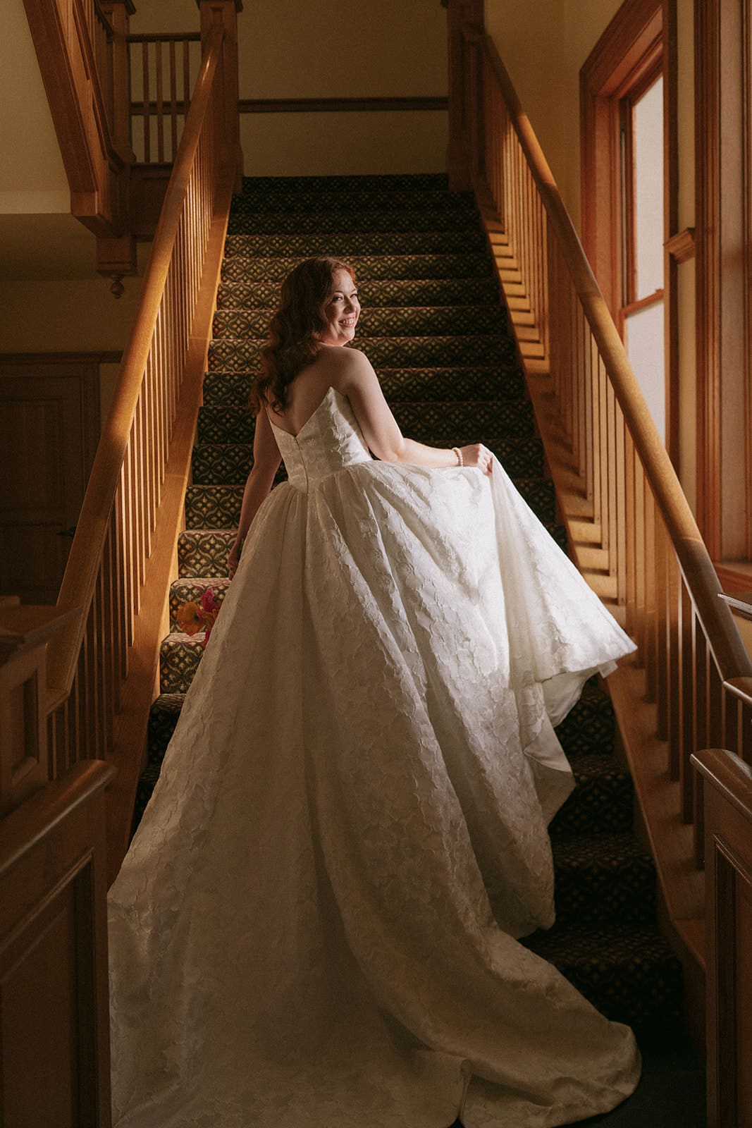 A person in a sleeveless, textured dress stands in the foreground with a group of people in dim lighting in the background for a wedding The Ashton Depot in Fort Worth