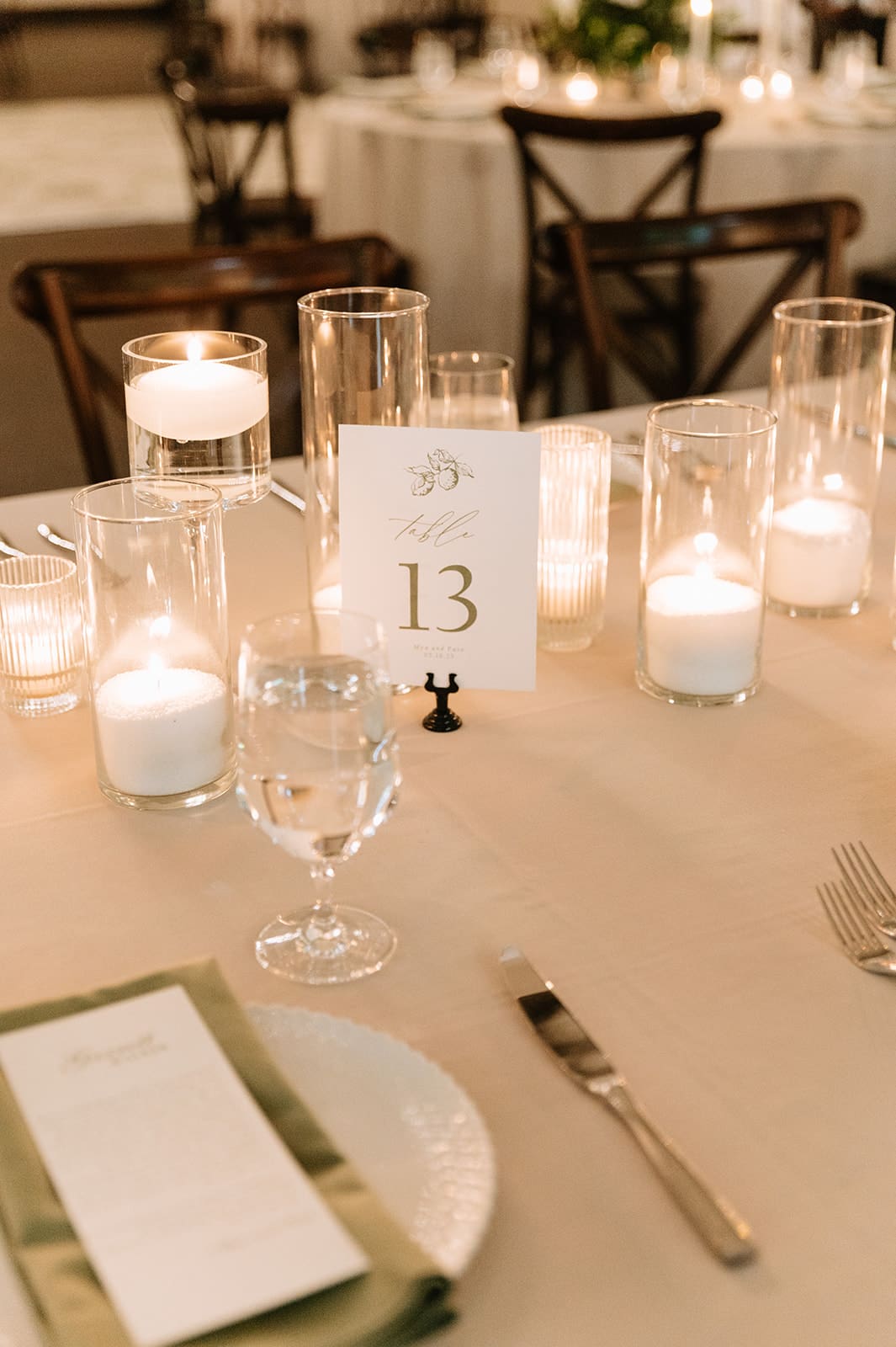 A long dining table set with plates, glassware, and lit candles, surrounded by wooden chairs and decorated with a white floral arrangement at The Springs Waxahachie