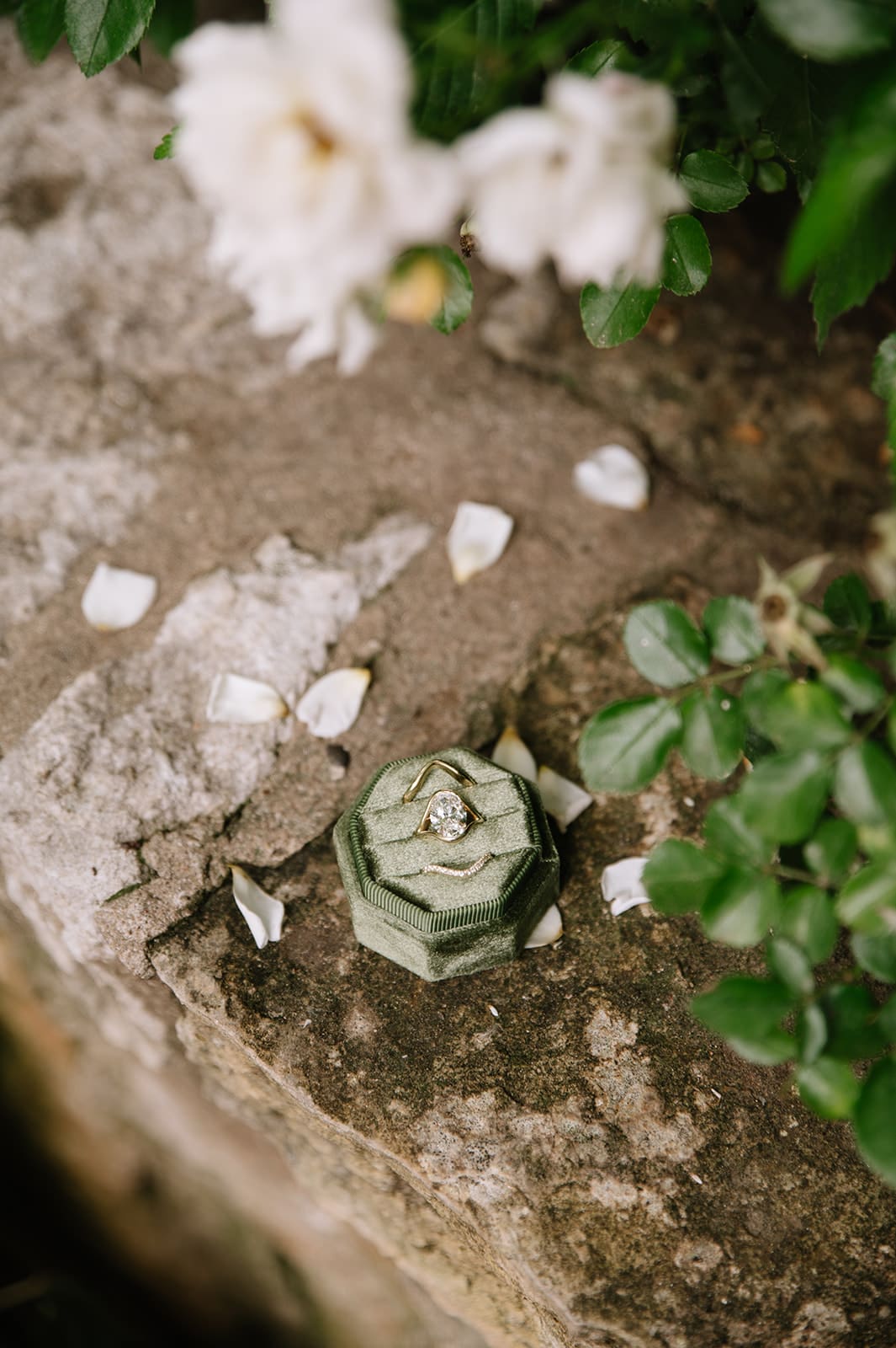 White high-heeled sandals, perfume bottles, jewelry, a black ring box, and a silver dish are arranged on a dark surface with white tulle fabric.
