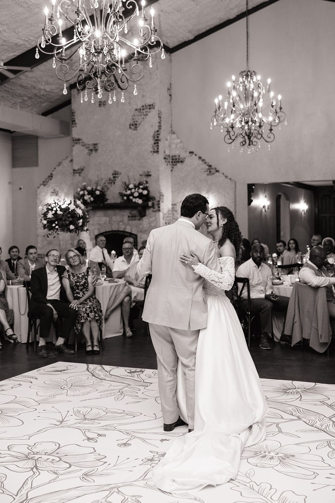 A bride in a white dress and a groom in a light blue suit share a dance at their wedding reception.