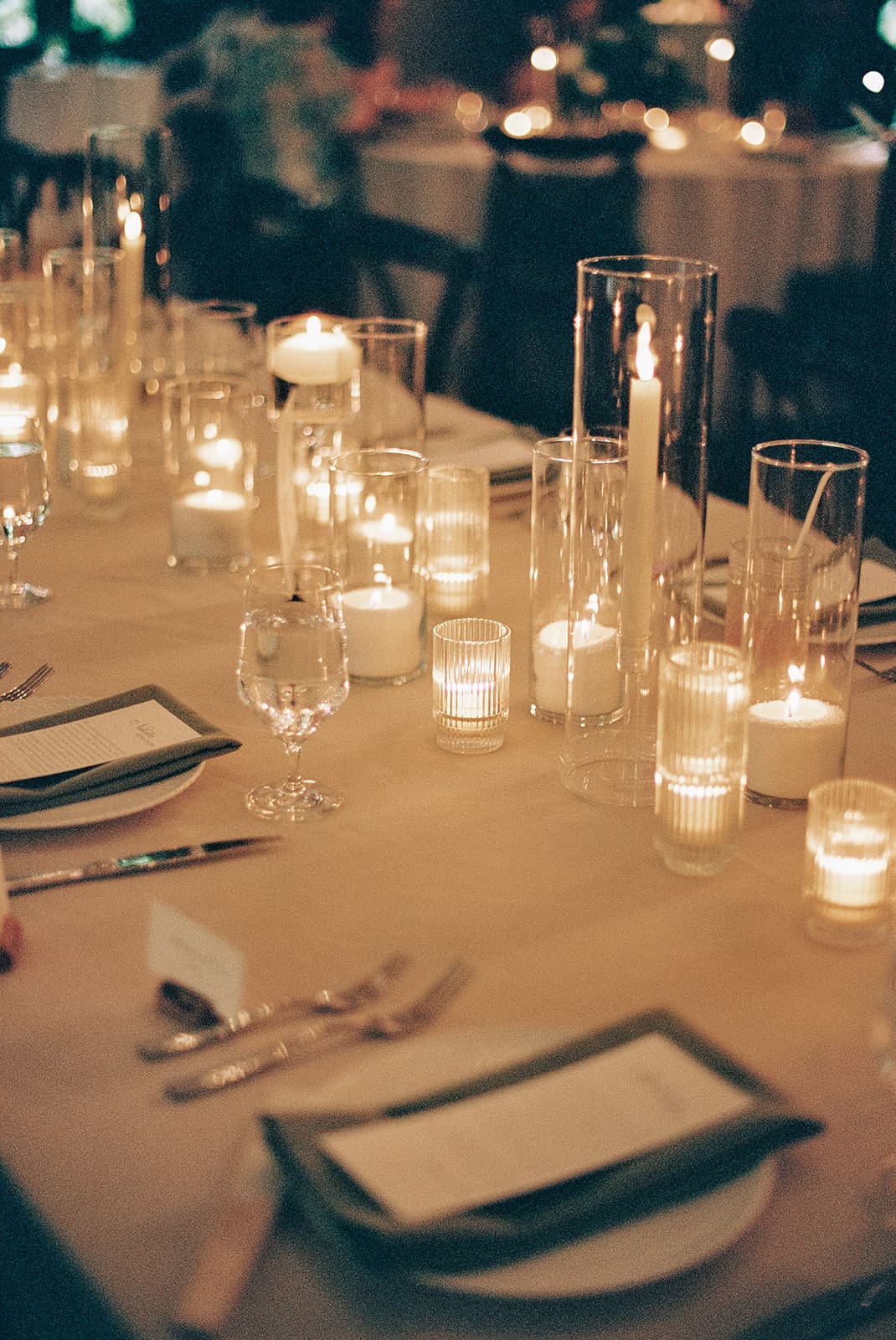 A long dining table set with plates, glassware, and lit candles, surrounded by wooden chairs and decorated with a white floral arrangement at The Springs Waxahachie