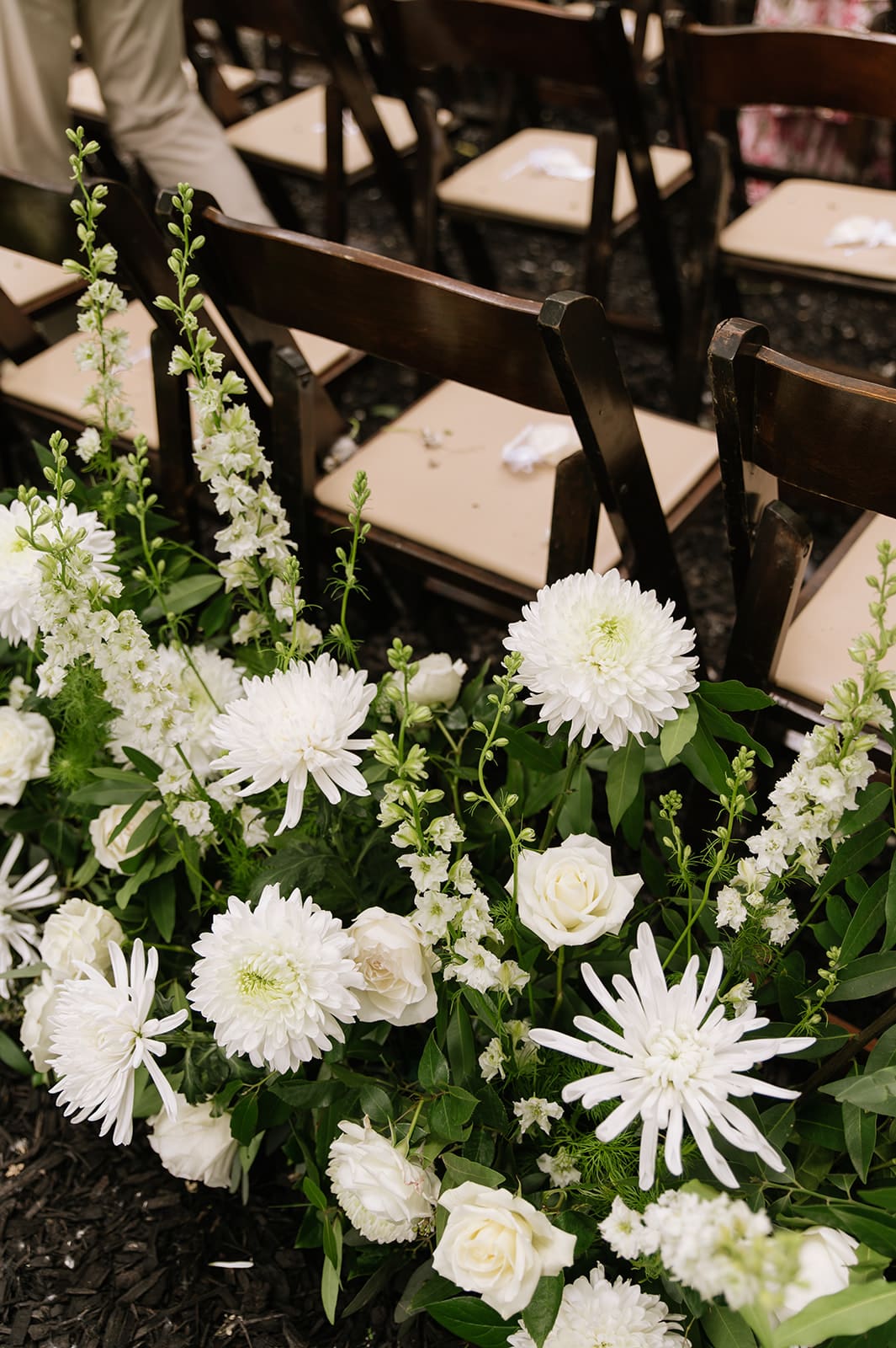 Rows of wooden chairs with beige seats are arranged behind a floral arrangement of white flowers and green leaves.