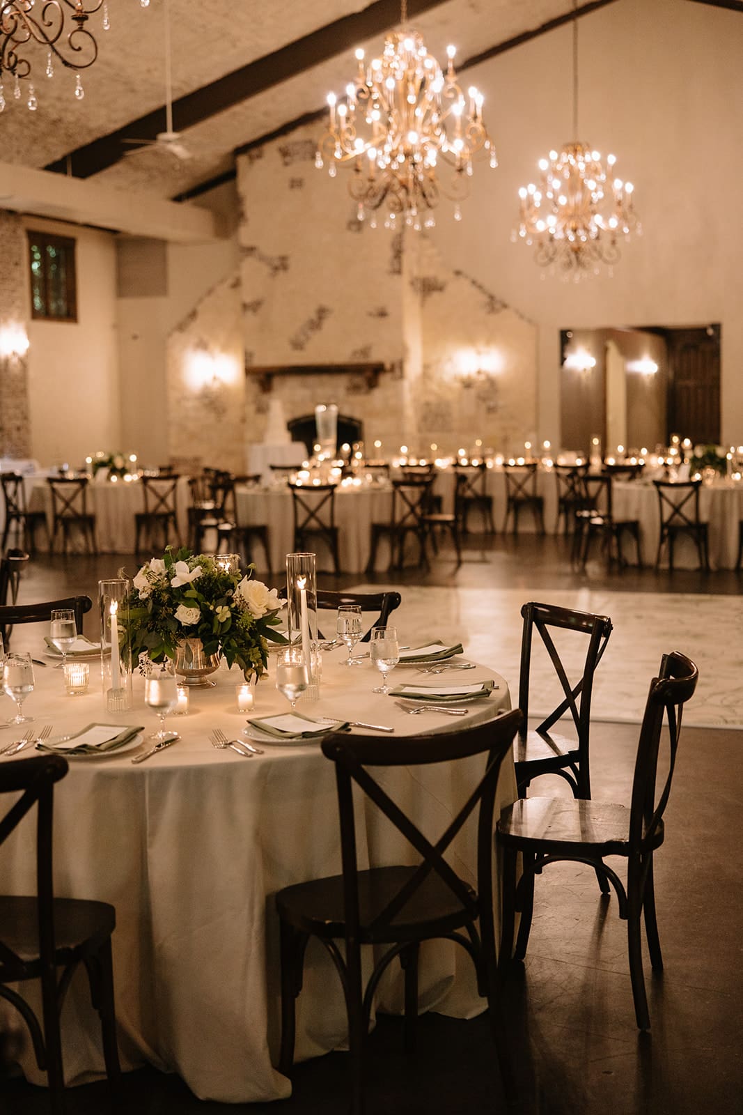 A long dining table set with plates, glassware, and lit candles, surrounded by wooden chairs and decorated with a white floral arrangement at The Springs Waxahachie