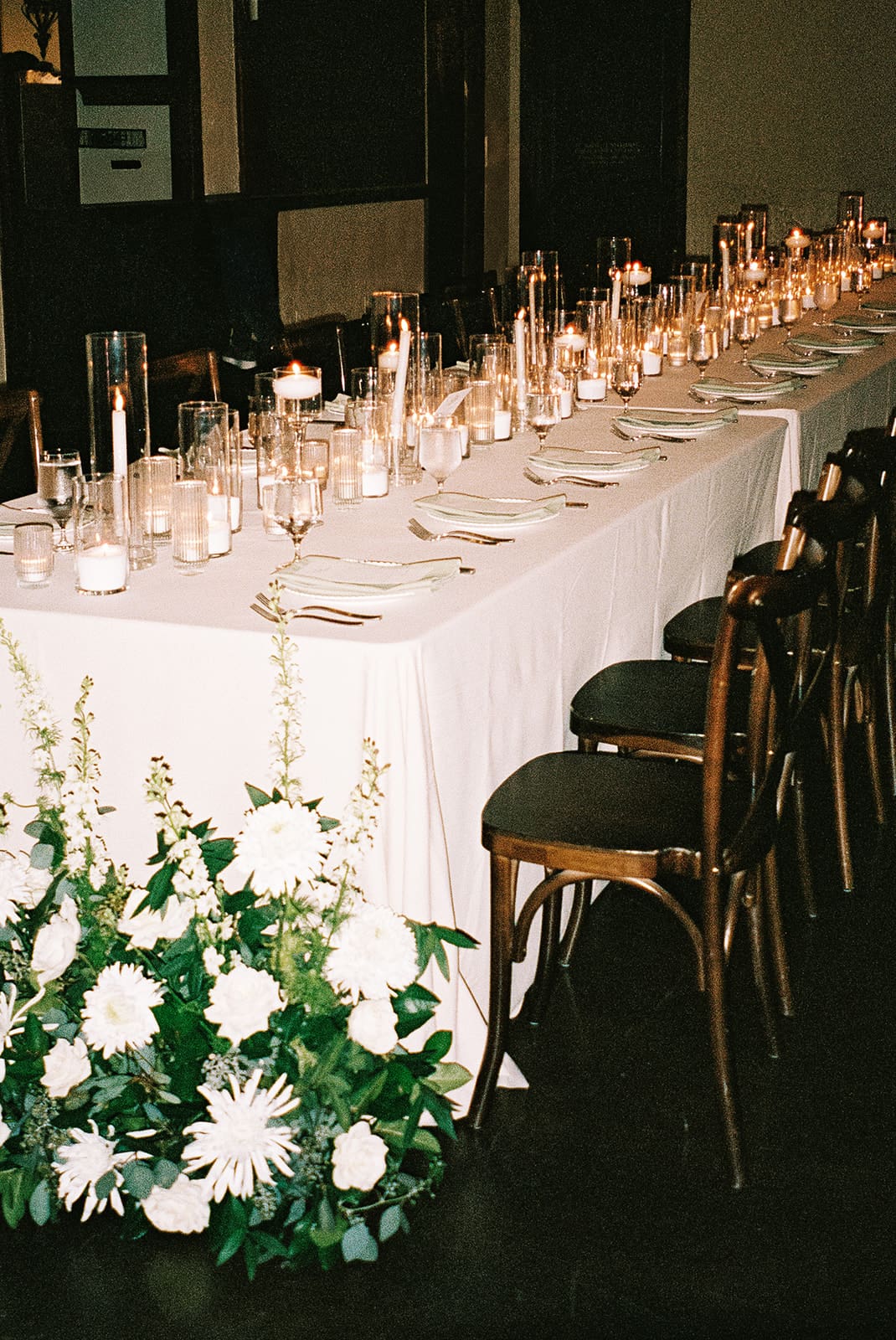 A long dining table set with plates, glassware, and lit candles, surrounded by wooden chairs and decorated with a white floral arrangement at The Springs Waxahachie