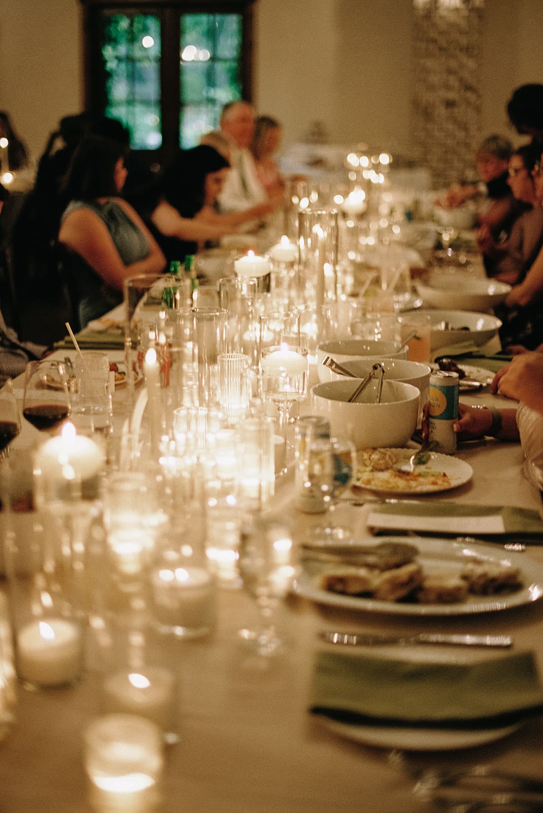 A long dining table set with plates, glassware, and lit candles, surrounded by wooden chairs and decorated with a white floral arrangement at The Springs Waxahachie