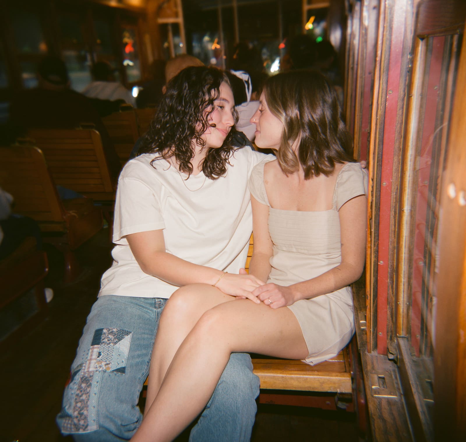 Two people sit closely together on a wooden bench, facing each other and making eye contact in a relaxed indoor setting for unique engagement photos