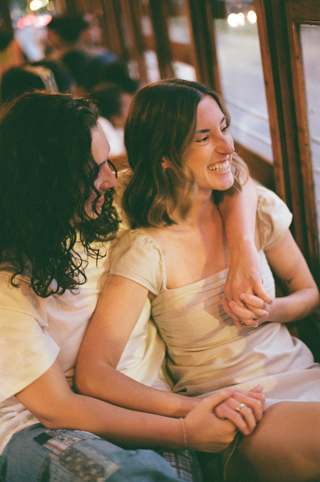 Two people sit closely together on a wooden bench, facing each other and making eye contact in a relaxed indoor setting for unique engagement photos