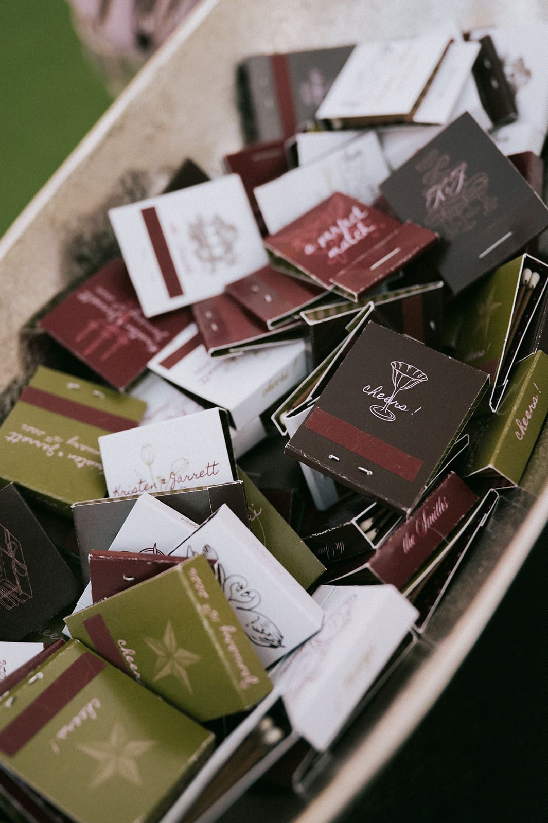 A close-up of a container filled with assorted matchbooks in green, white, black, and burgundy colors, each displaying various printed designs and text.