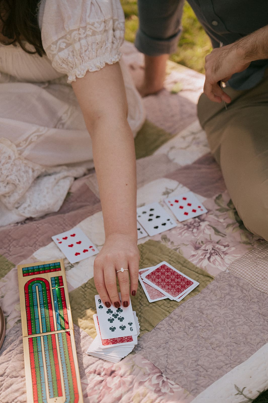 Two people sitting close together, holding playing cards with red backs, one person wearing a white lace dress.