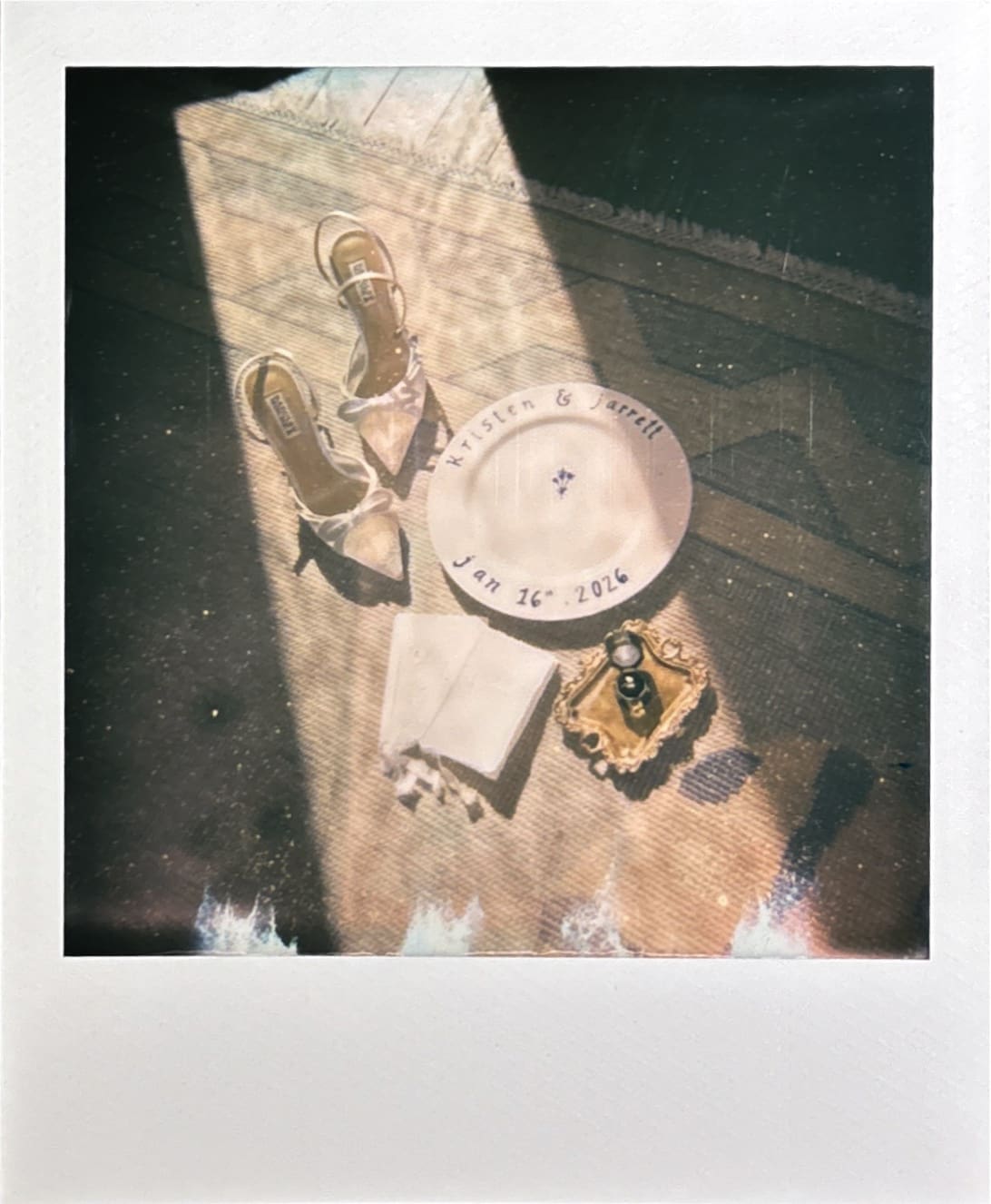 A pair of sandals, a plate with text, a folded napkin, and a small purse are arranged on a sunlit surface.