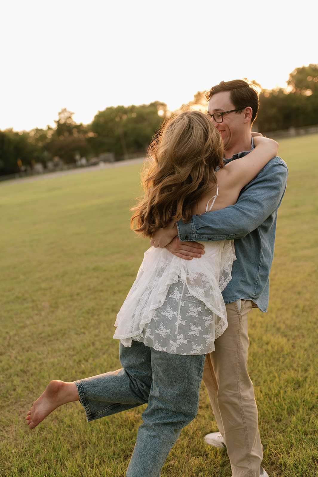 A man and a woman sit on a picnic blanket on the grass, facing each other and talking, with a hill and trees in the background for unique engagement pictures