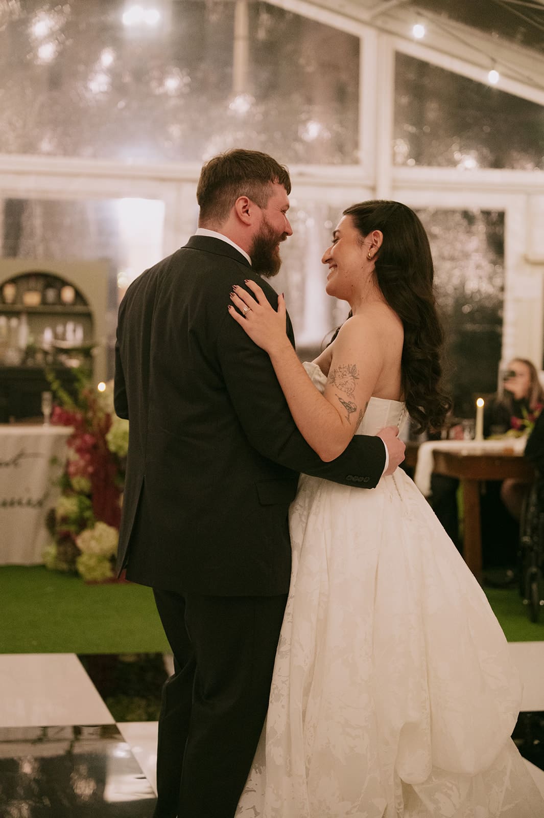 A bride and groom dance together at their wedding reception, smiling and holding each other in a warmly lit venue.