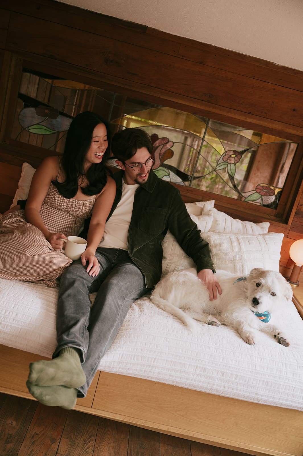 A woman and man dance together in a kitchen while a white dog stands nearby, looking up at them for their unique engagement photos