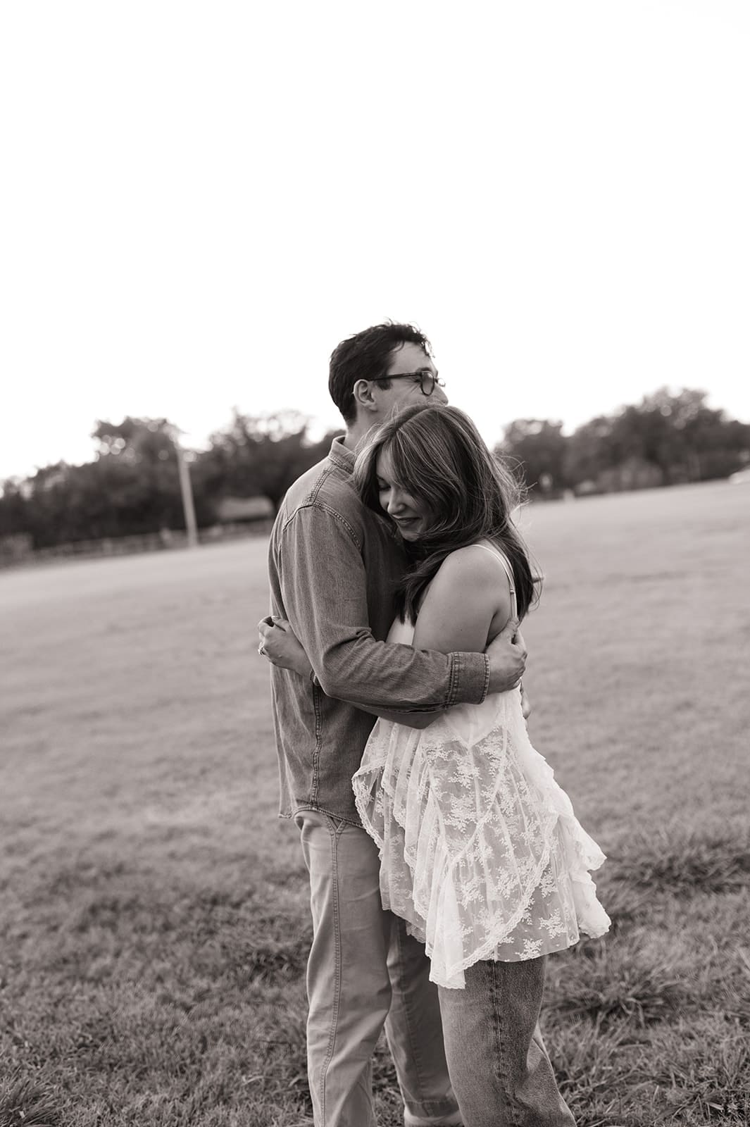 A man and a woman sit on a picnic blanket on the grass, facing each other and talking, with a hill and trees in the background for unique engagement pictures