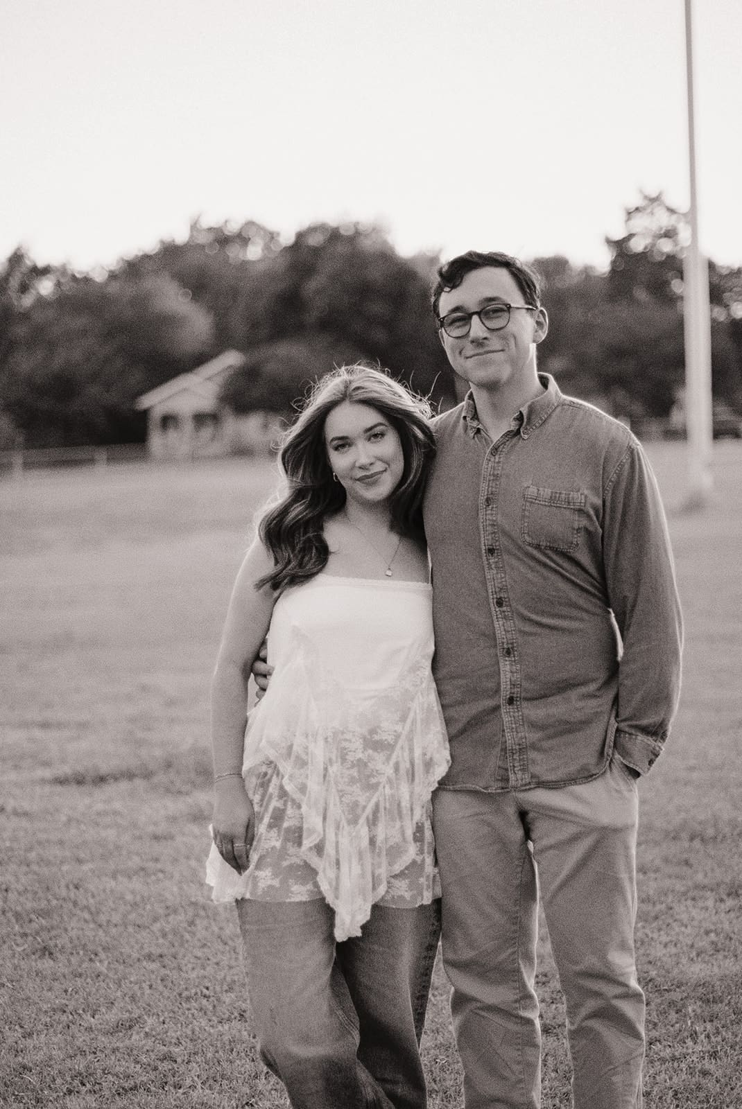 A man and a woman stand next to each other with a hill and trees in the background for unique engagement pictures