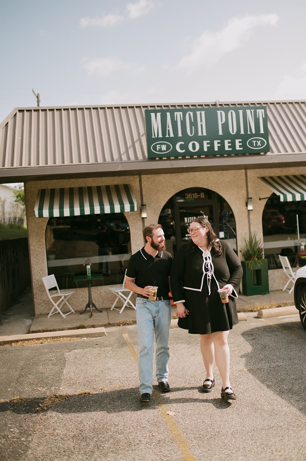 Two people sit at a small table outside Match Point Coffee, a café with striped green and white awnings and a large sign above the entrance.