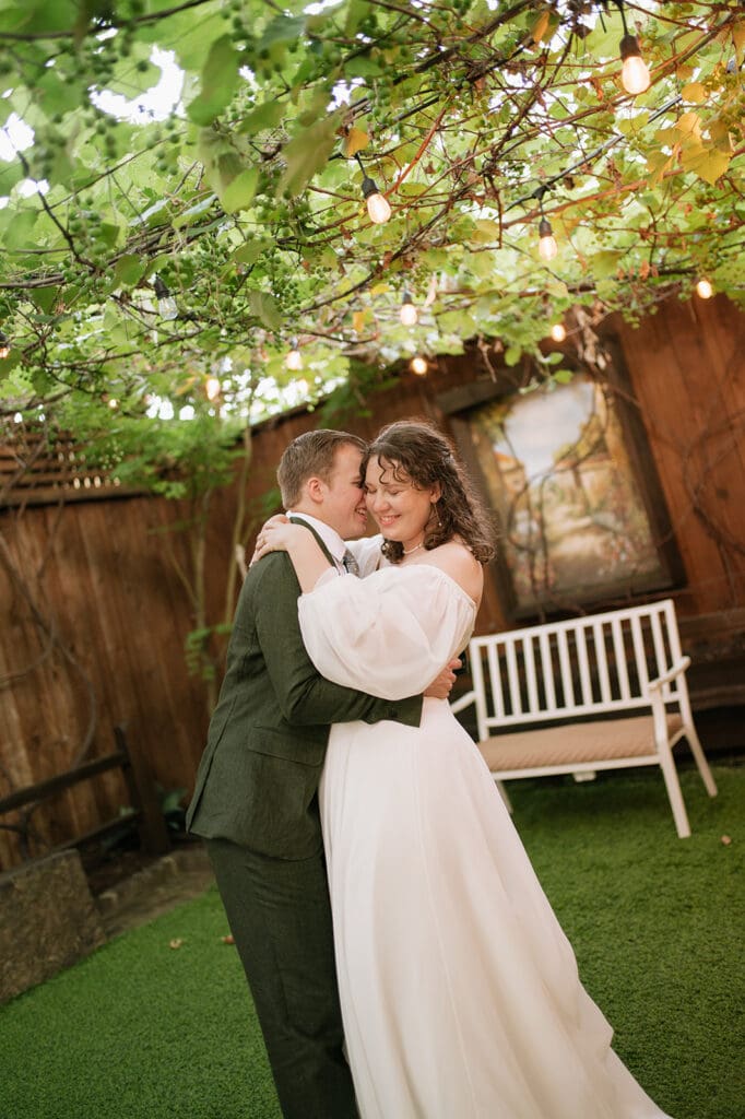 A bride and groom embrace and smile at each other under string lights in an outdoor garden setting at Magnolia Terrace in Frisco, Tx