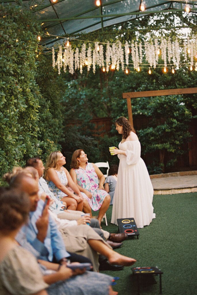 Three women sit on grass in a circle, interacting with a colorful xylophone. White folding chairs and greenery are in the background at Magnolia Terrace in Frisco, Tx