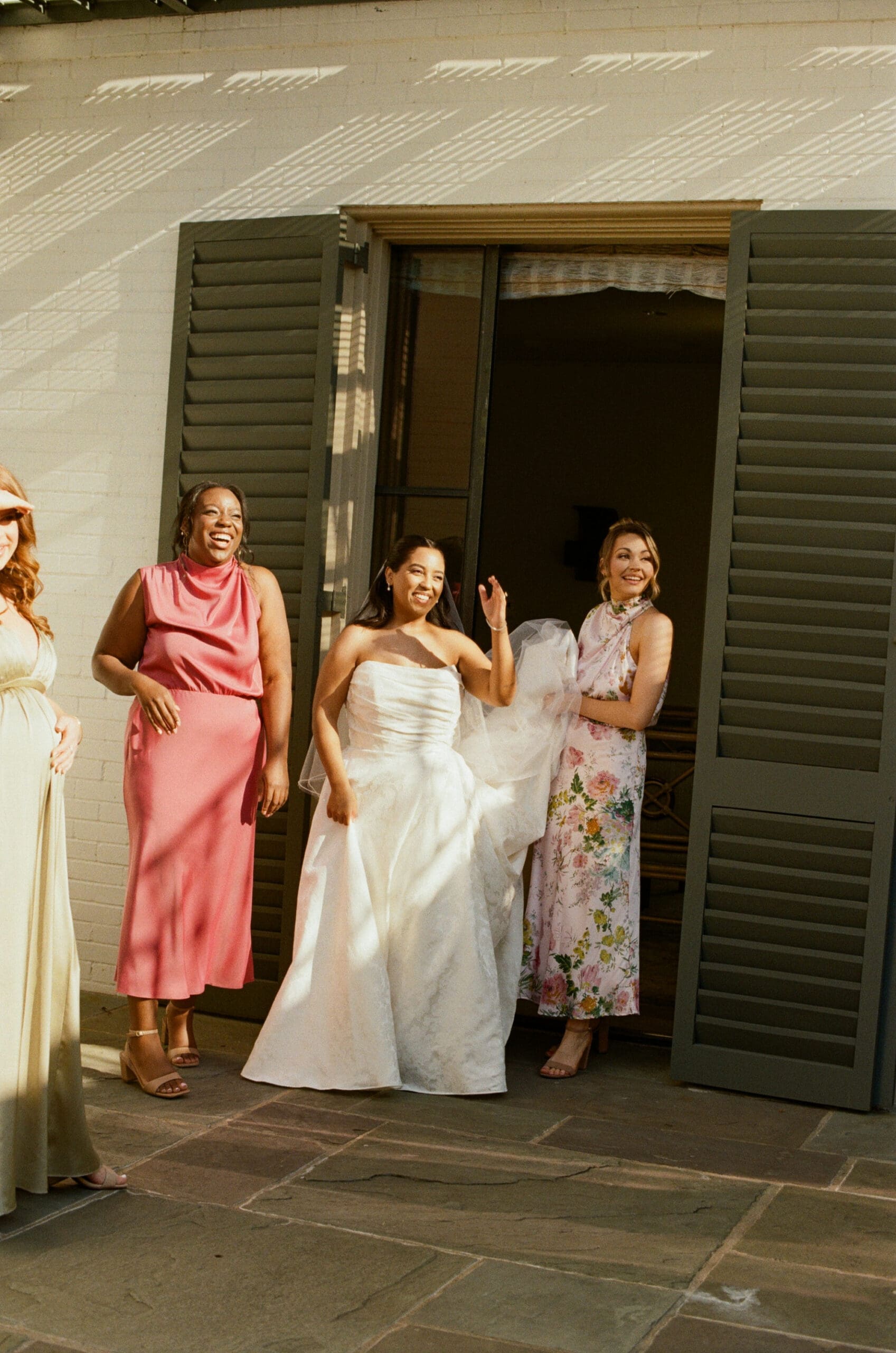 first look with bridesmaids on film in the morning sunlight as bridesmaid holds brides dress train